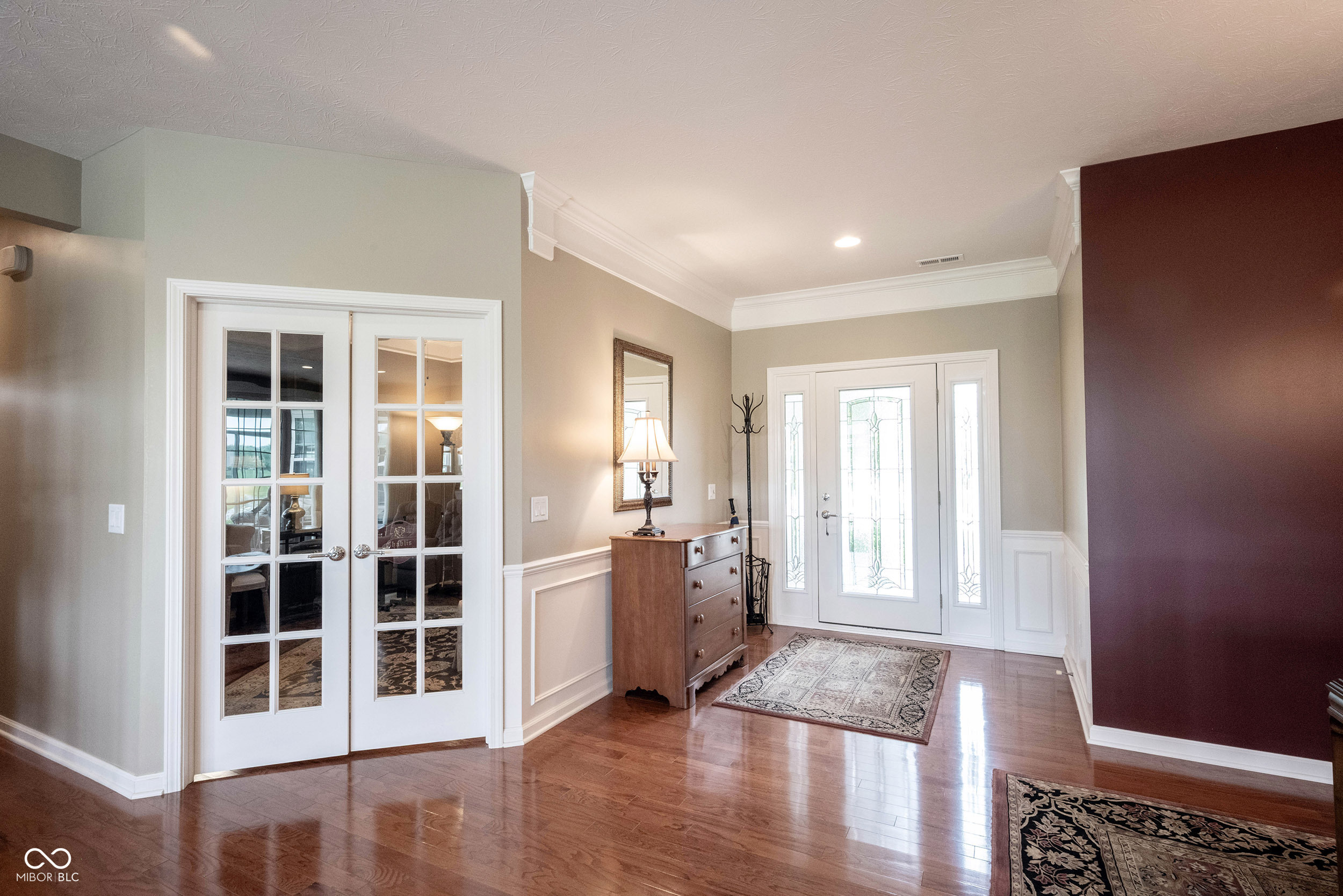 Entry foyer with glass-paneled front door, hardwood floors, patterned rugs, and a wooden chest beneath a mirror.