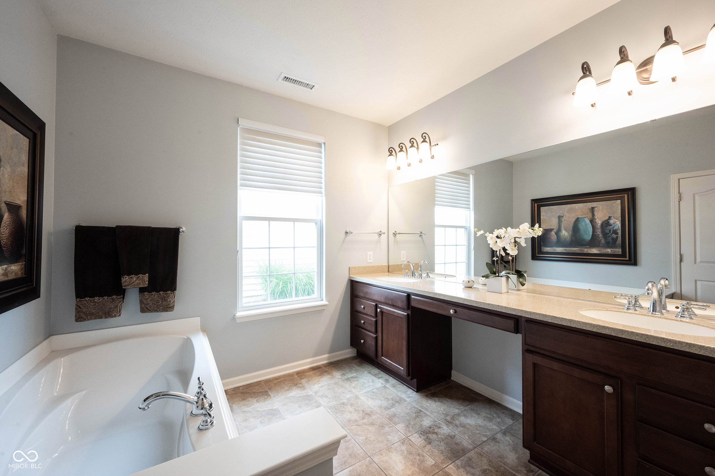 Bathroom with a soaking tub and long double vanity beneath a large mirror.