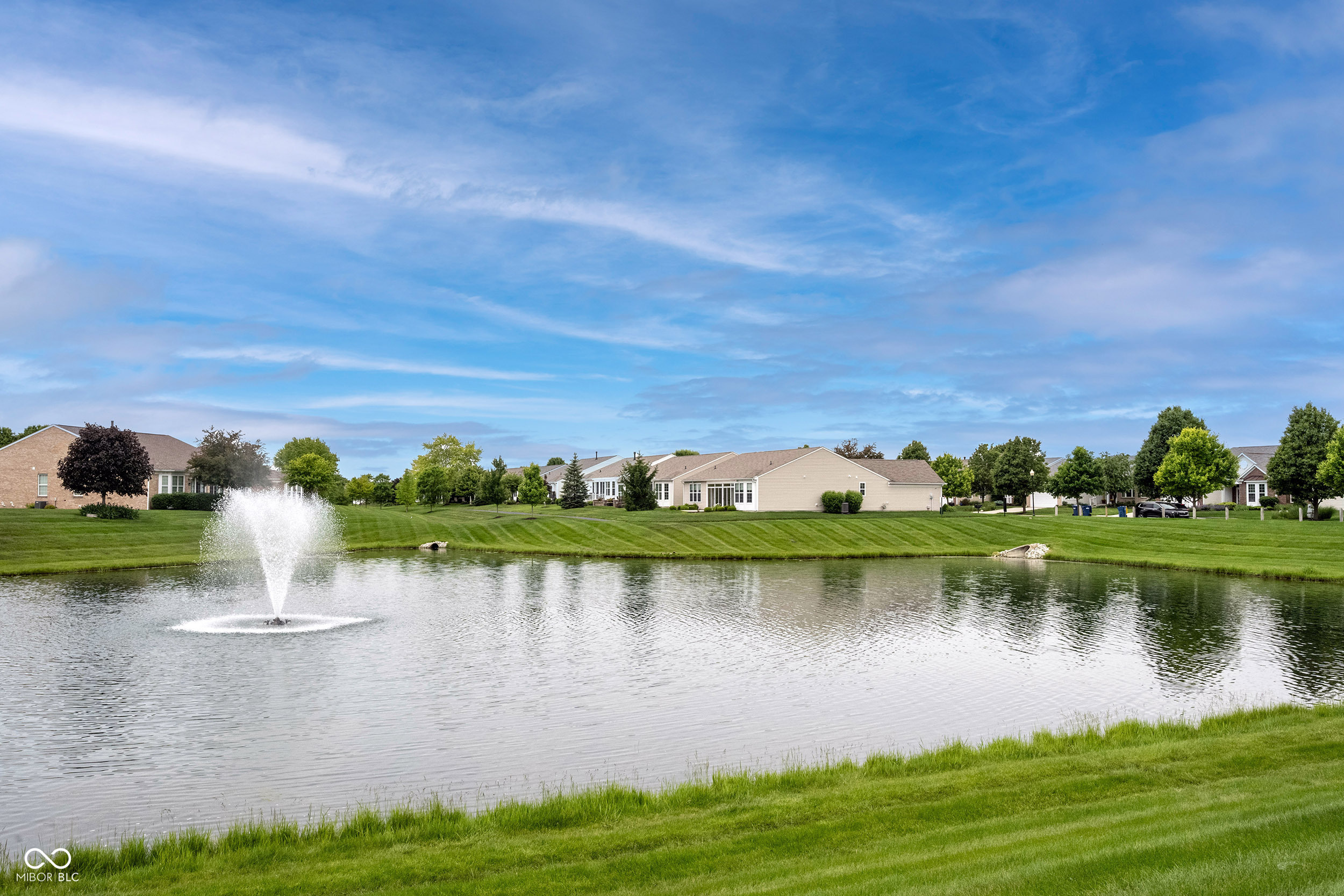 Neighborhood homes across a pond with a fountain and manicured green lawns.