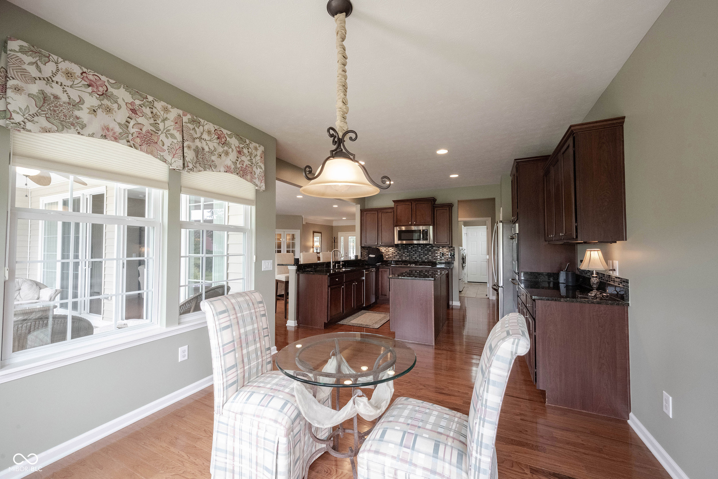 Kitchen and dining area with dark wood cabinetry, a glass table, plaid chairs, and large windows.