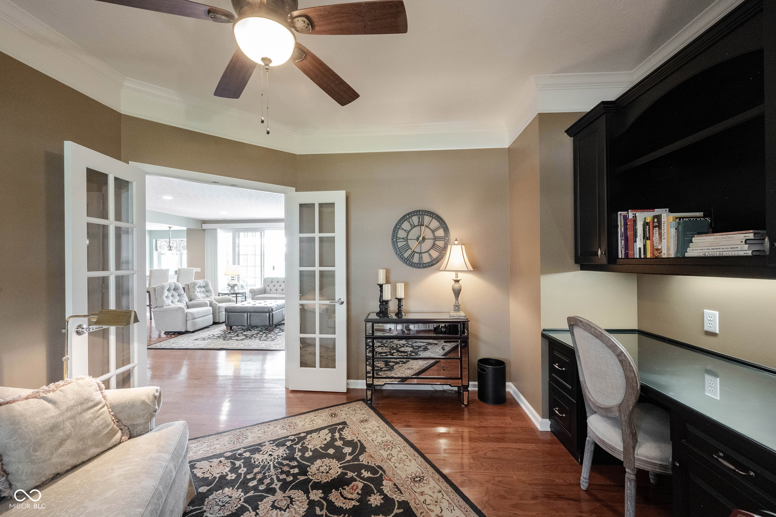 Home office with built-in desk and shelving, patterned rug, and French doors to the living room.