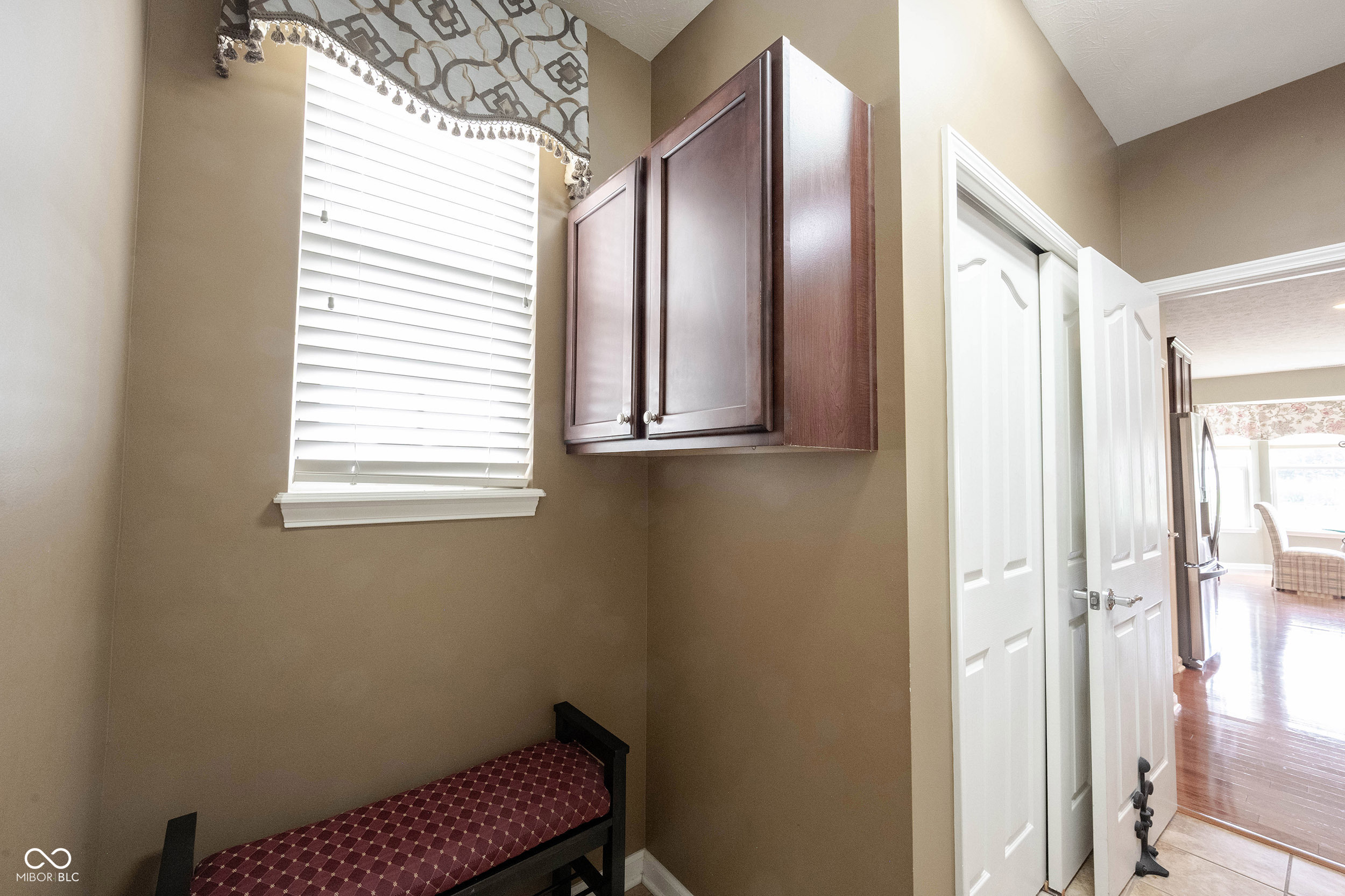 Small room with a burgundy-cushioned bench, wall cabinets, and a window beside an open doorway.