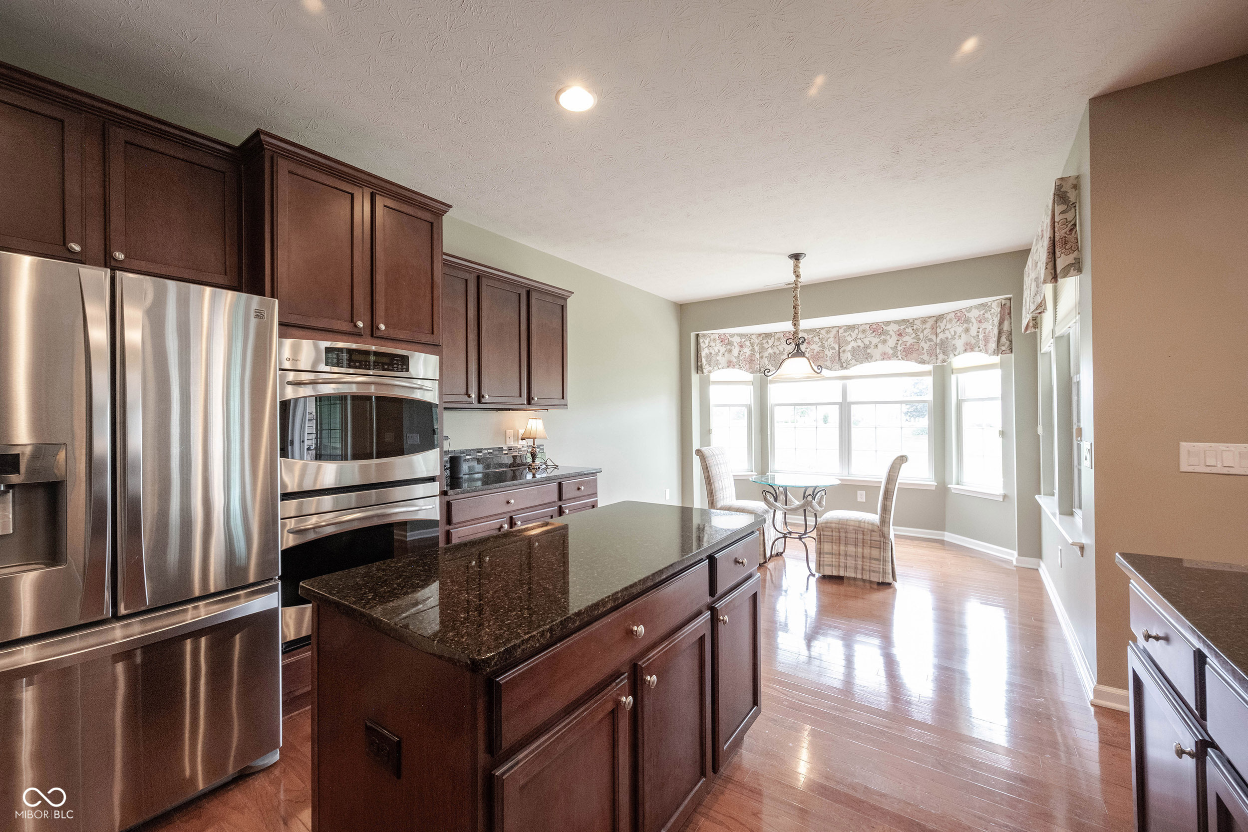 Kitchen with dark cherry cabinetry, stainless appliances, granite island, and a bright window-side breakfast nook.