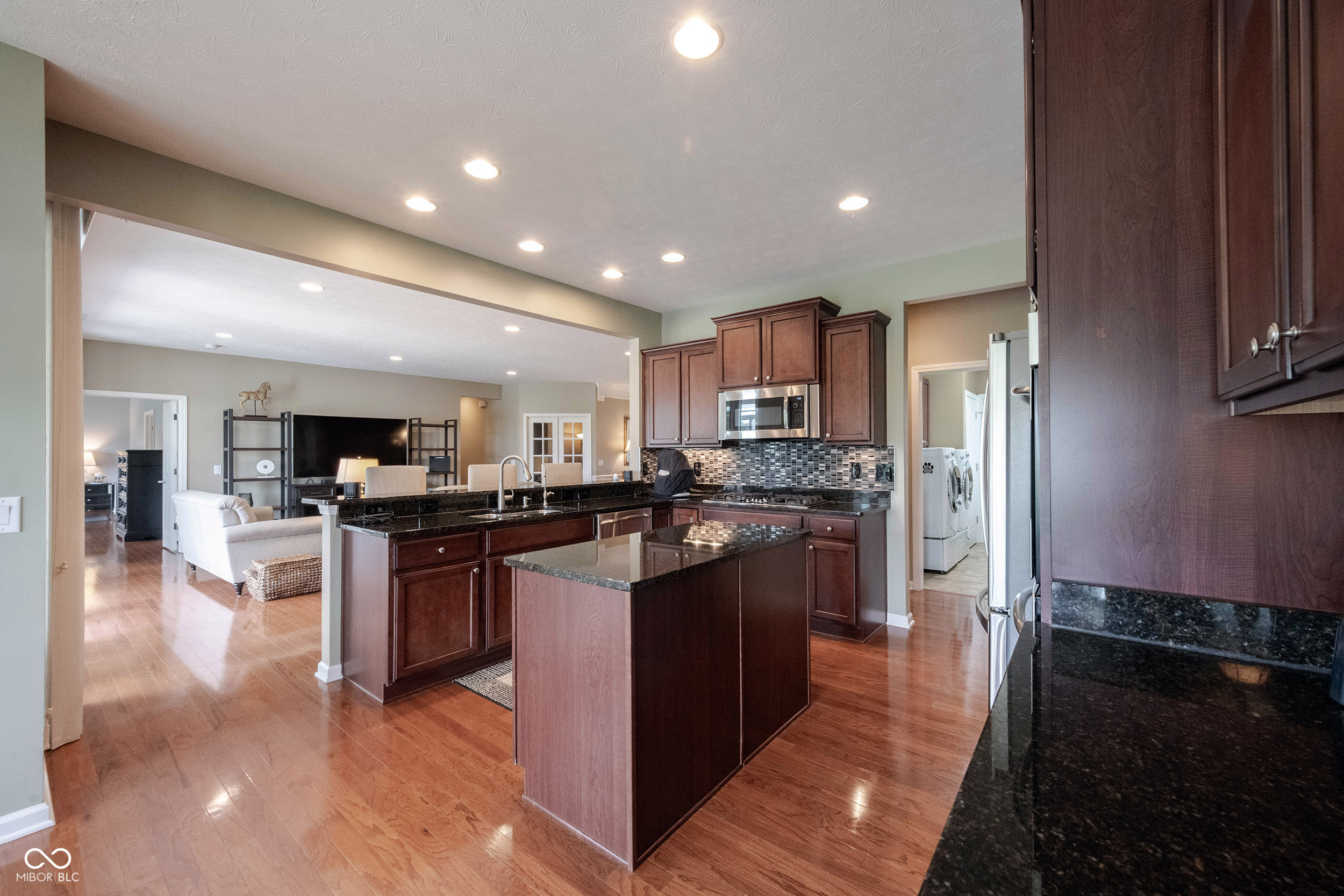 Kitchen with dark wood cabinets, granite counters, a central island, and an open view into the living area.