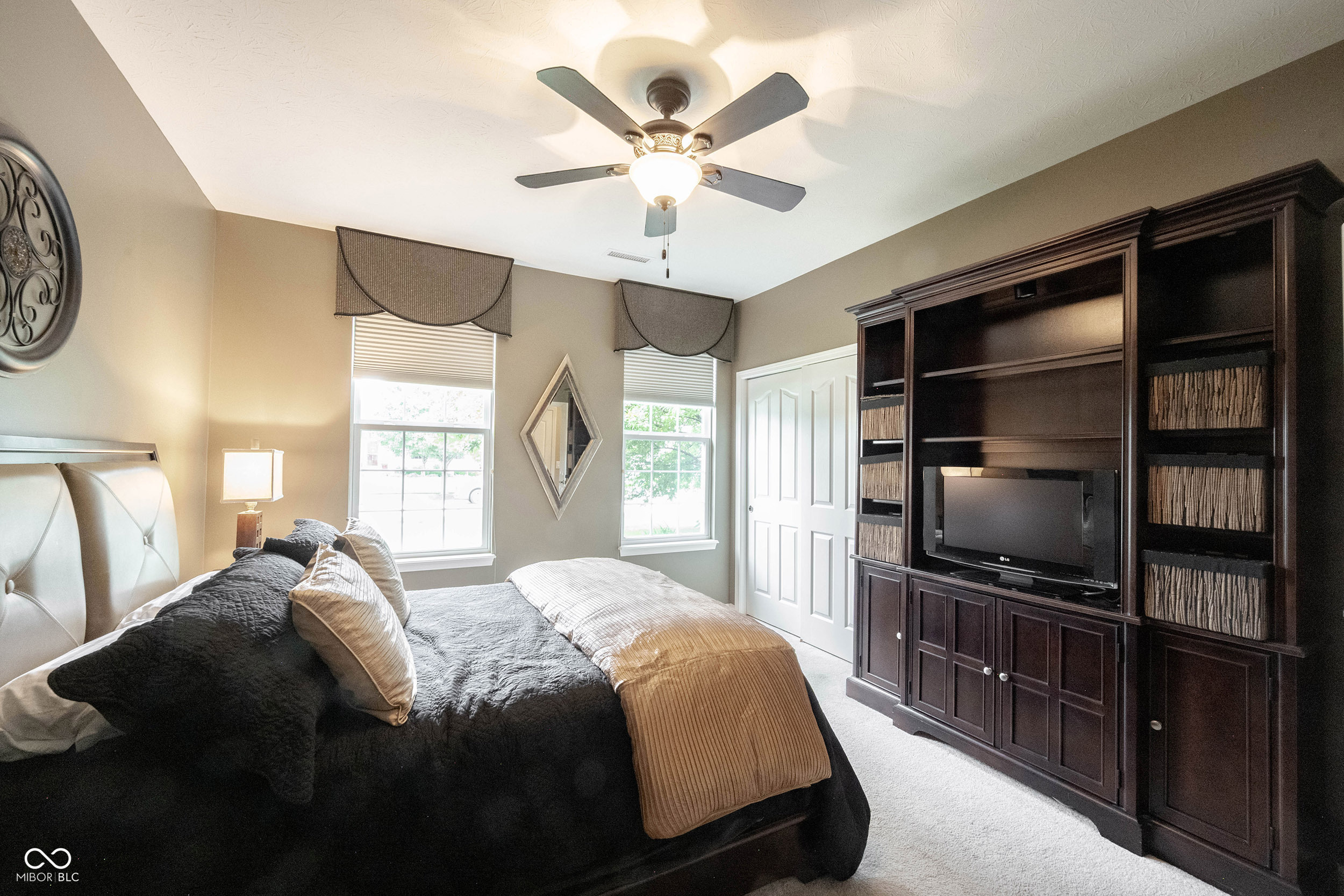 Bedroom with a dark bed, built-in entertainment cabinetry, two windows, and a ceiling fan.