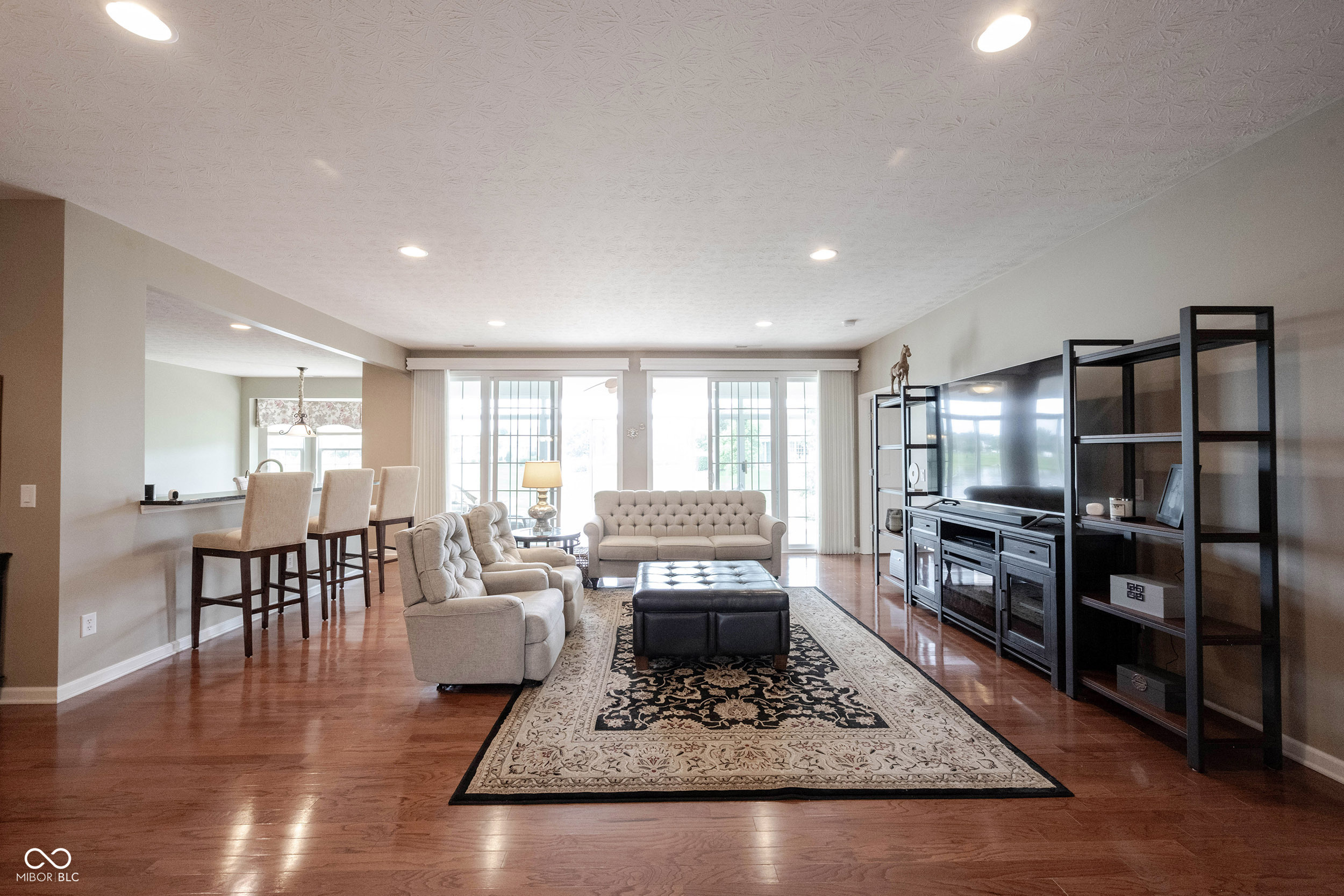 Furnished living room with hardwood floors, tufted sofas, patterned rug, and black entertainment unit.
