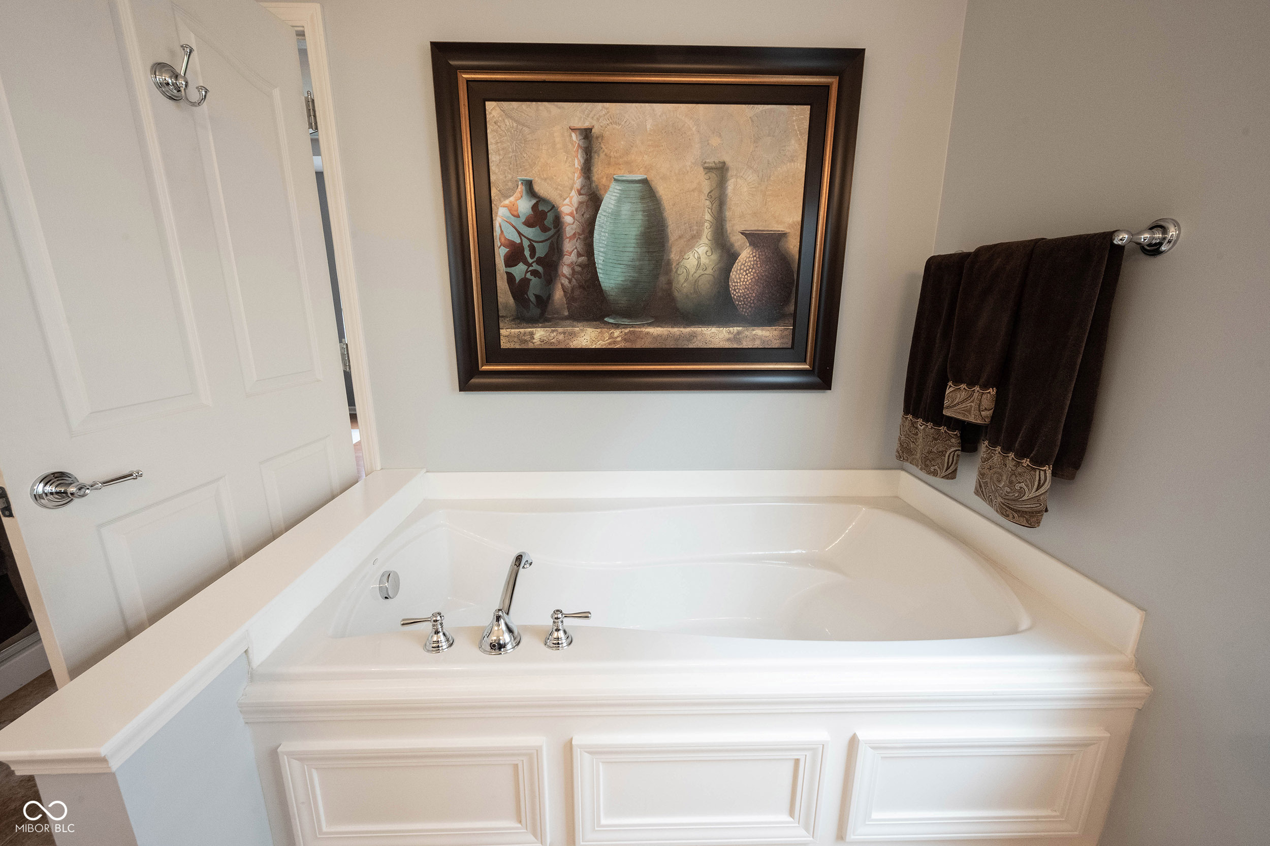 Bathroom with a large white corner soaking tub, chrome fixtures, and framed artwork.