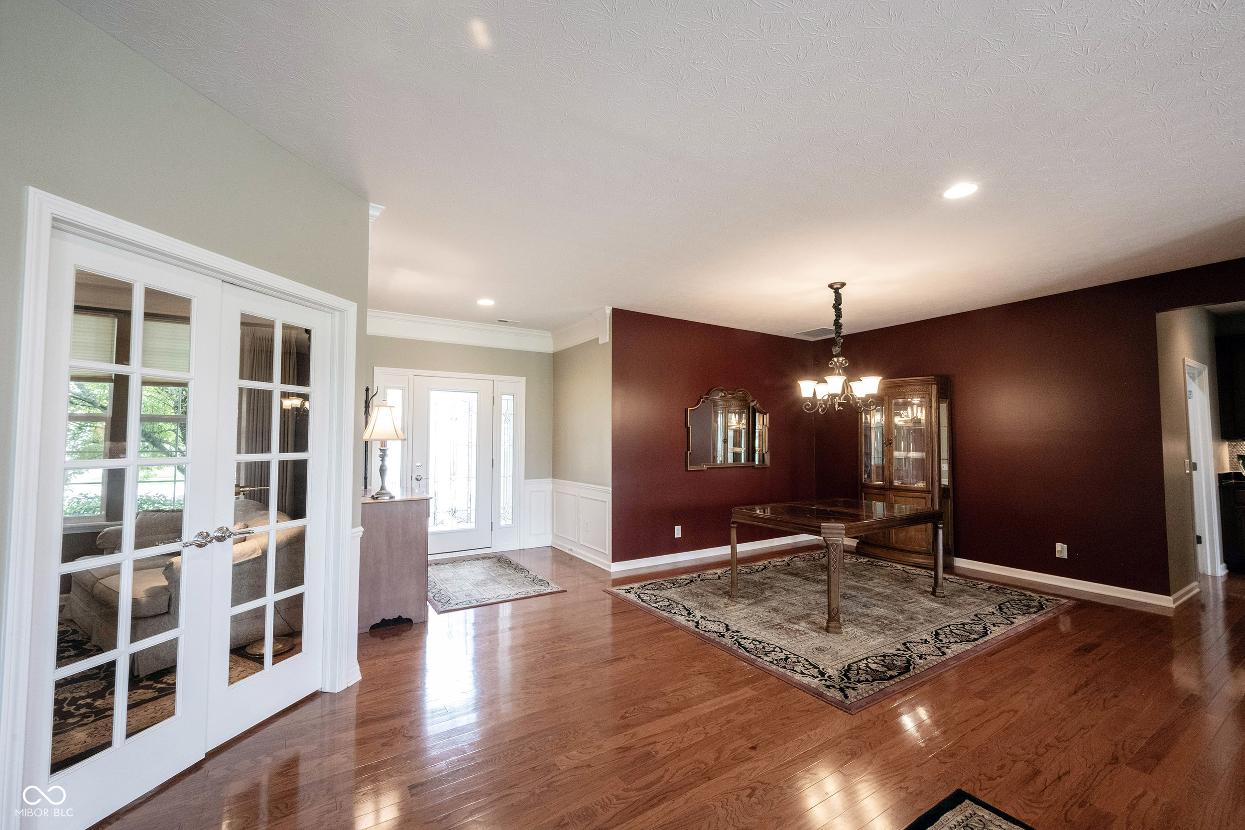Formal dining room with a red accent wall, hardwood floors, and a wooden table beneath a chandelier.
