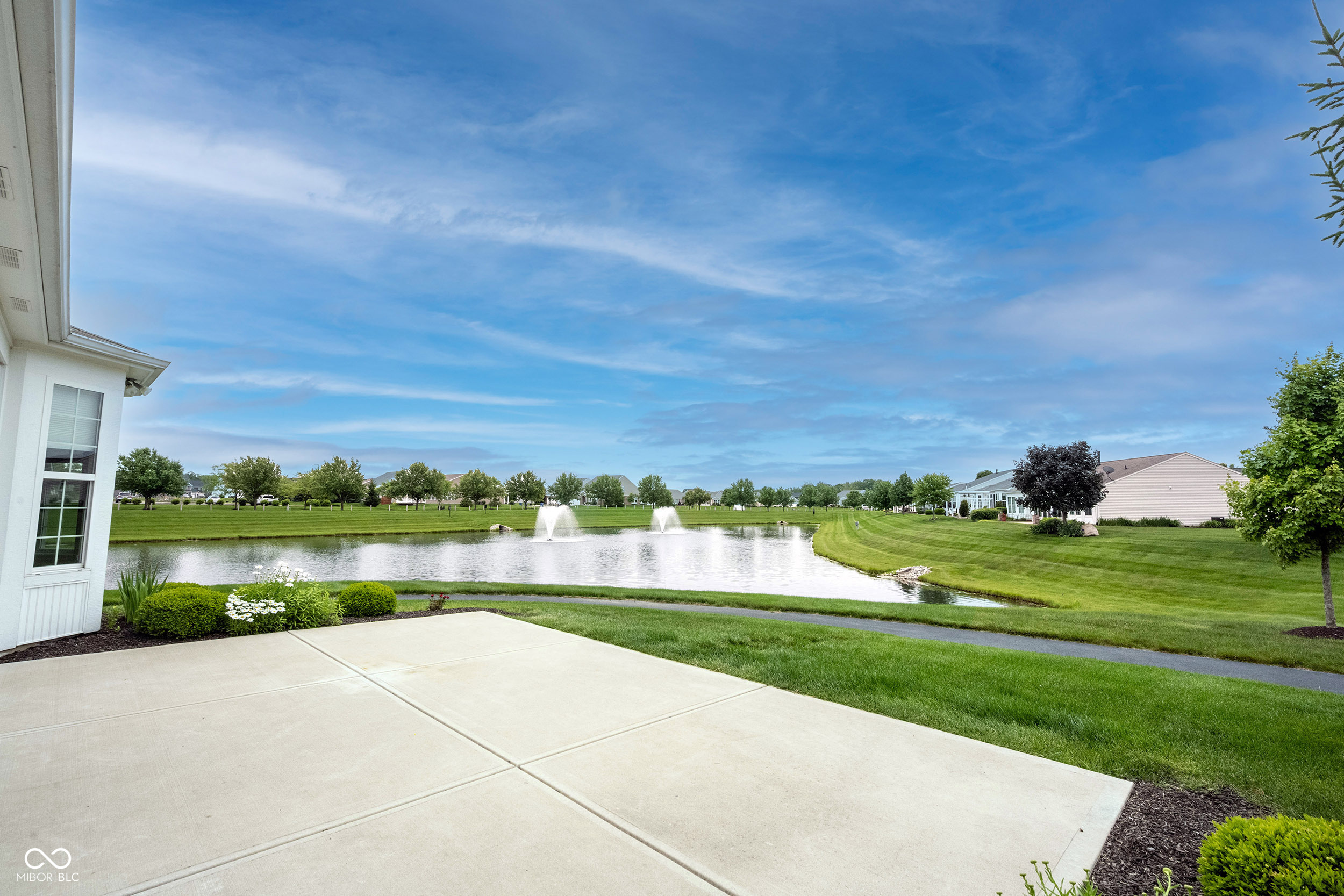 Patio overlooking a landscaped pond with two fountains and manicured lawns.