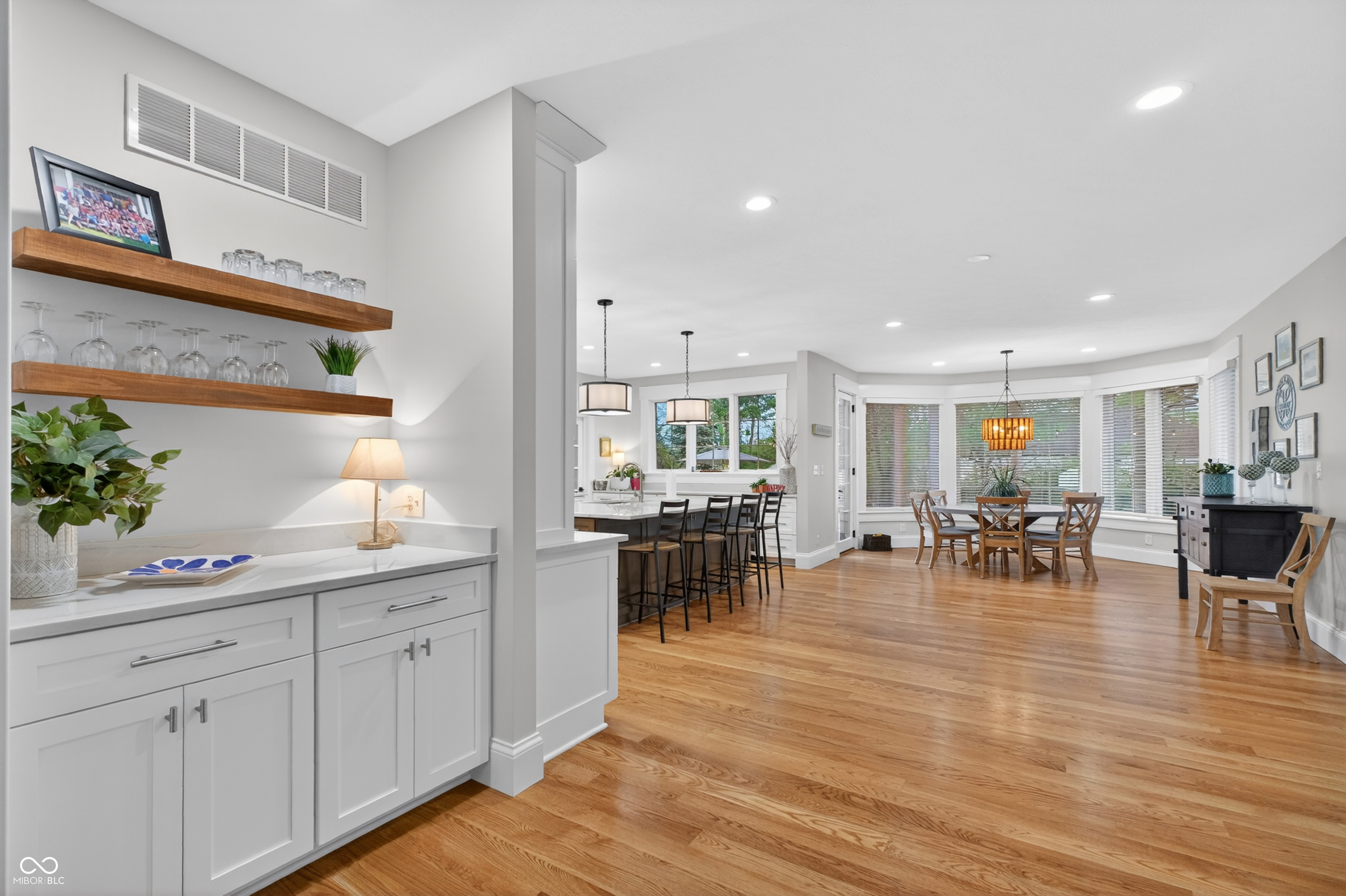 Open kitchen and dining area with floating wood shelves, breakfast bar, bay windows, and hardwood floors.