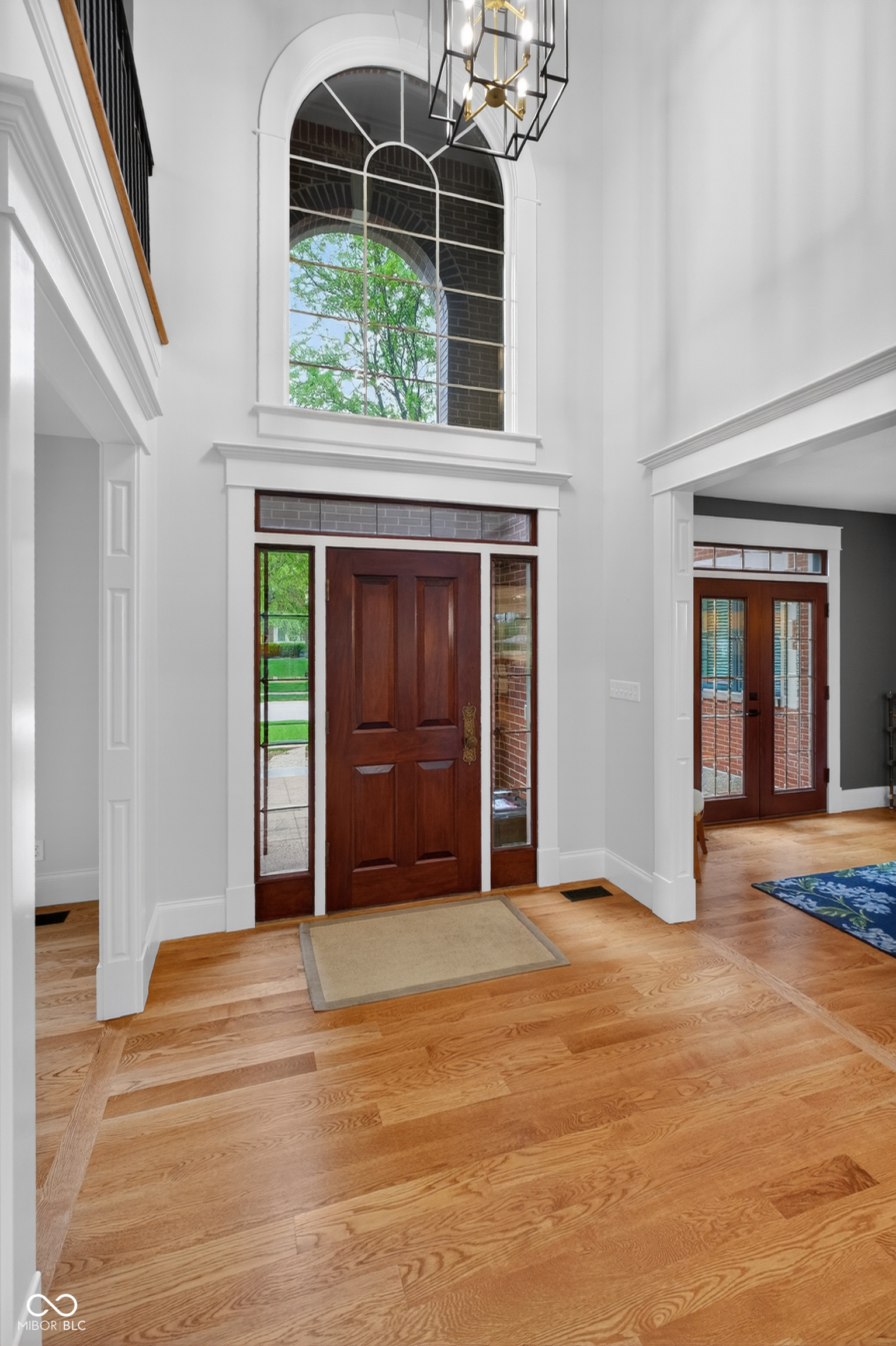 Two-story entry foyer with a dark wood front door, arched window, and hardwood floors.