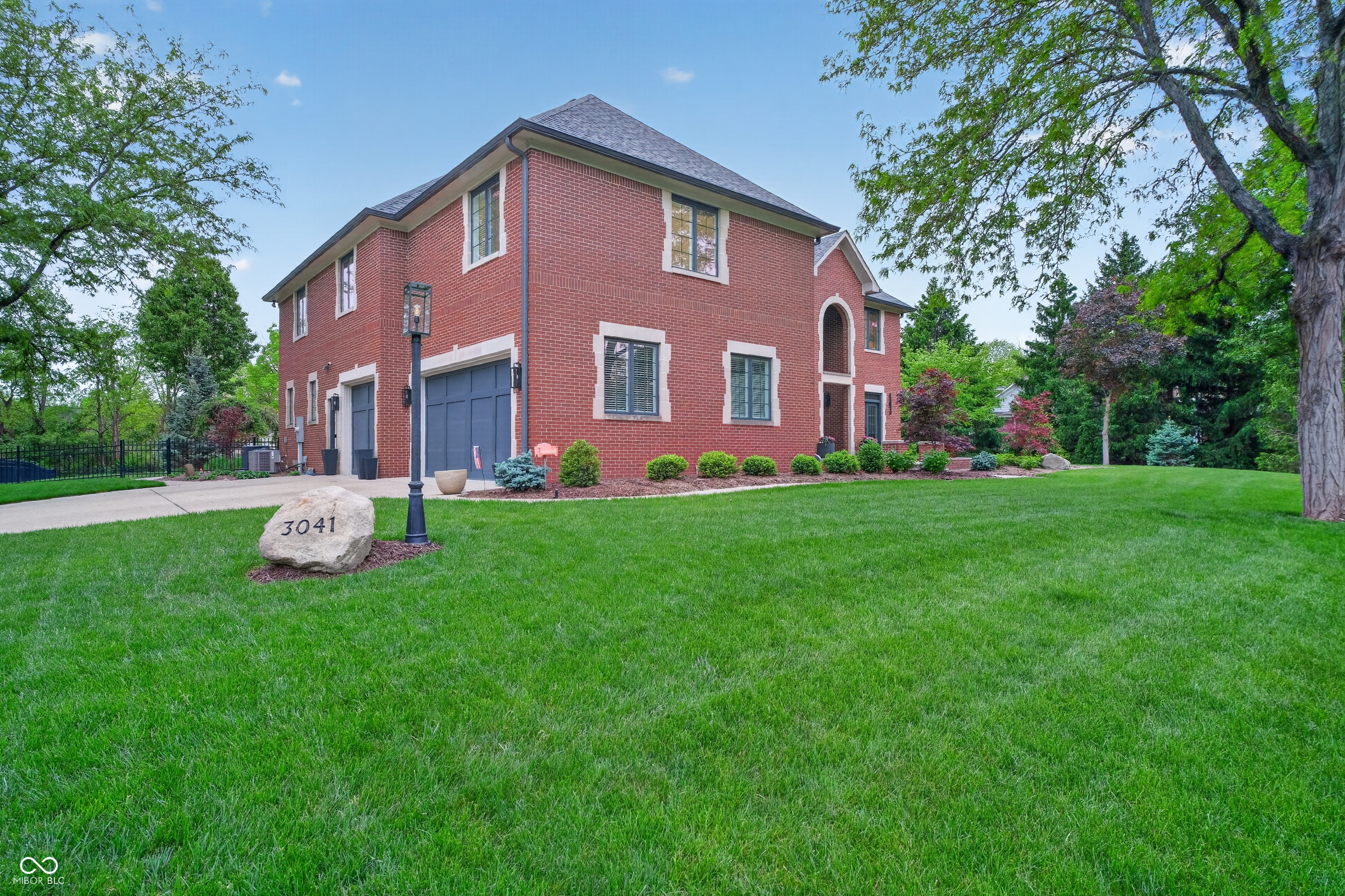 Two-story red brick house with gray garage doors, landscaped shrubs, and a lawn bearing a 3041 address marker.