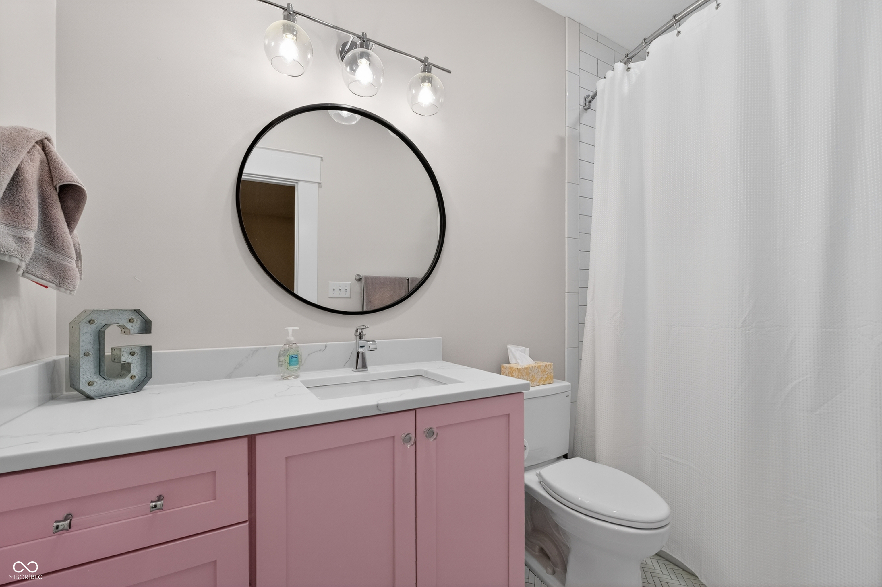 Bathroom with a pink vanity, round mirror, white countertop, and shower curtain.