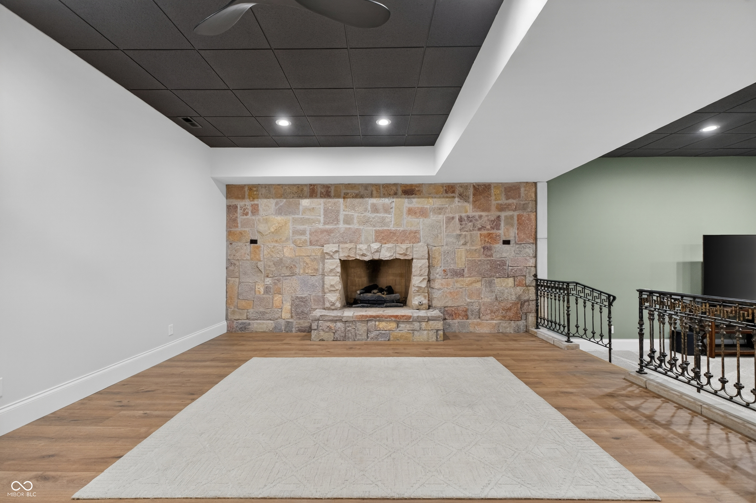 Interior room with a large stone fireplace, wood floors, and a light rug.