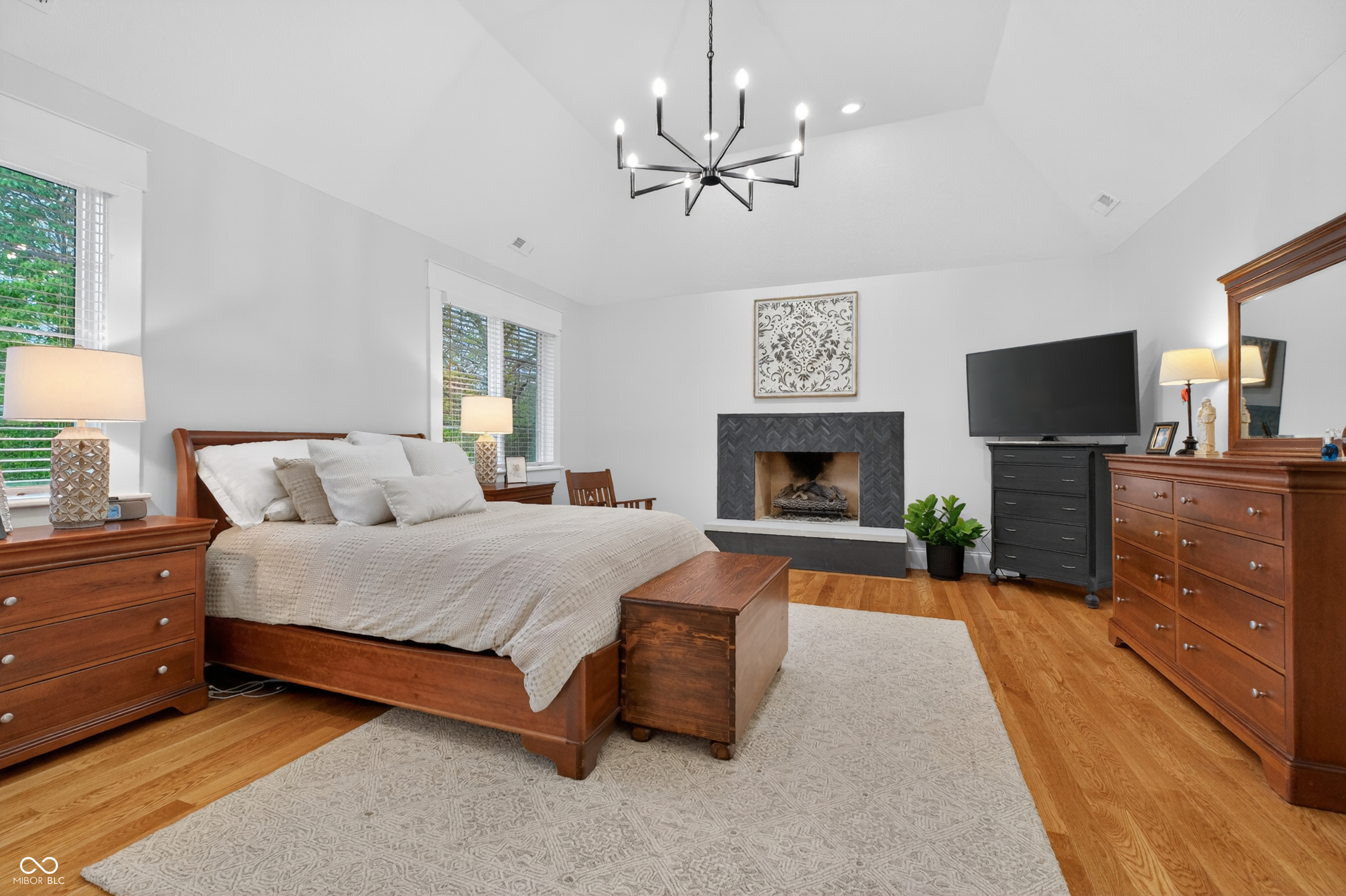 Furnished bedroom with a wood bed, hardwood floors, and a dark tiled fireplace.
