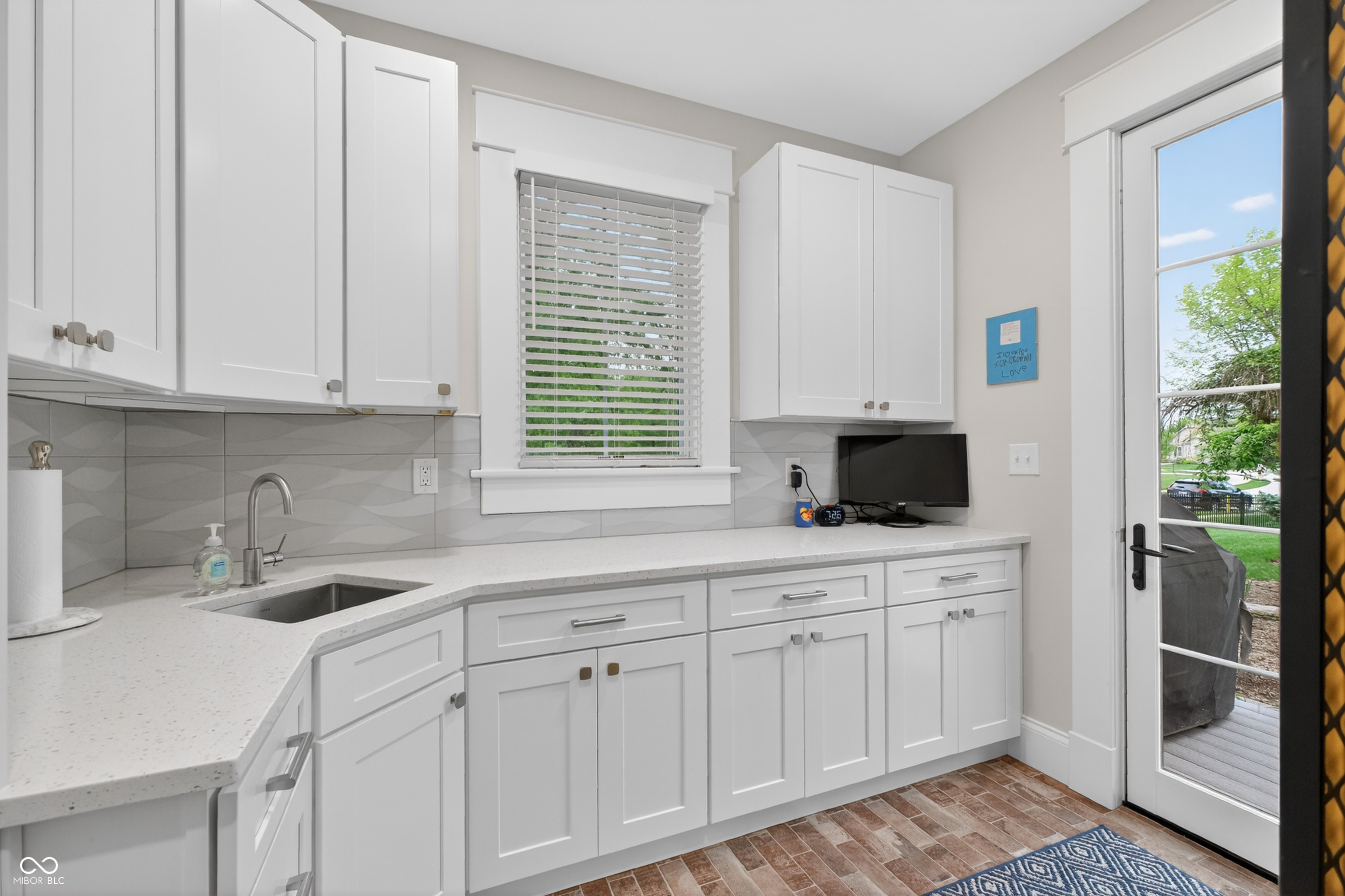 Kitchen with white cabinets, geometric tile backsplash, and a glass door opening to a deck.