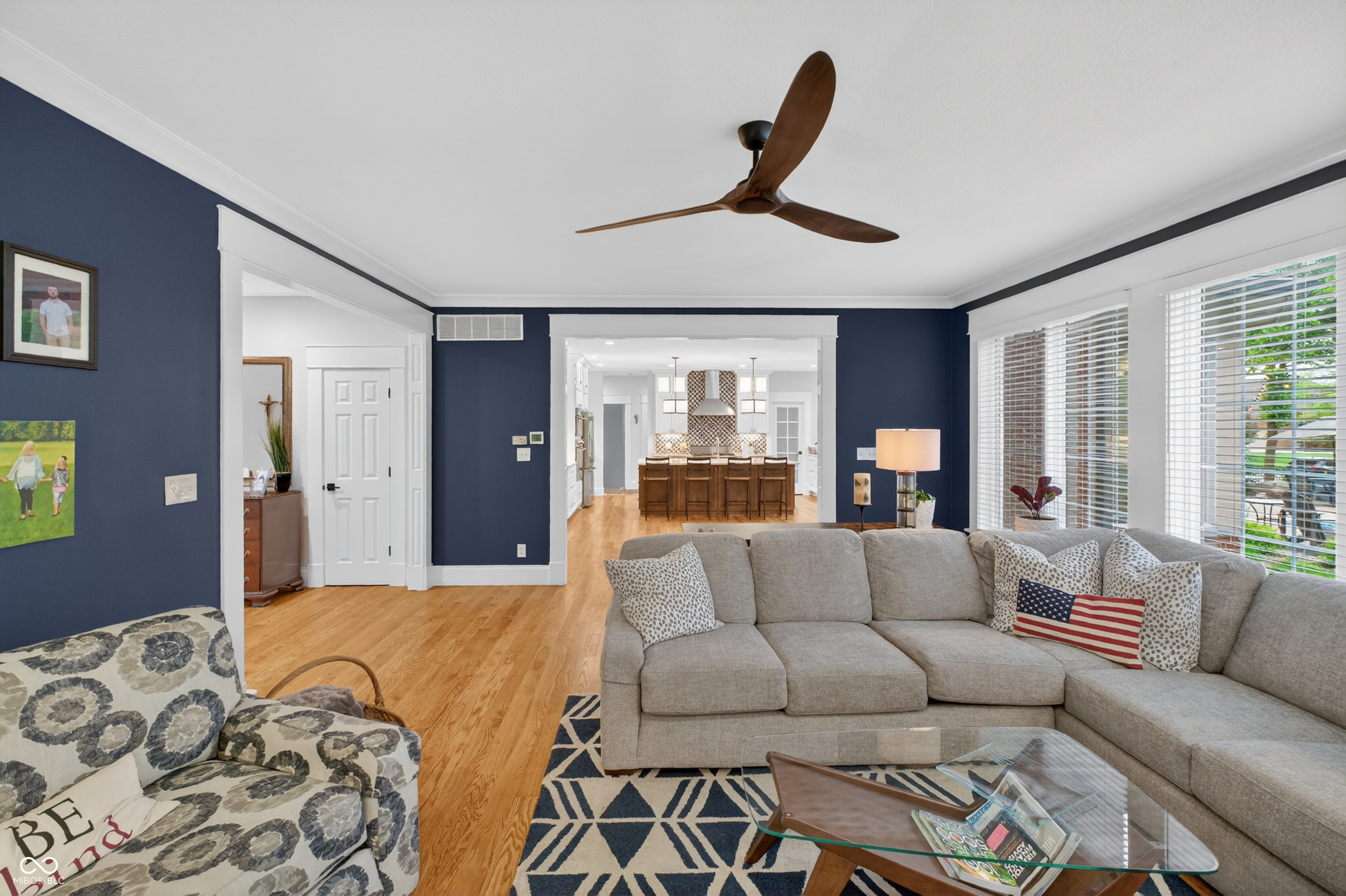 Furnished living room with navy walls, a gray sectional, patterned armchair, and view into the kitchen.