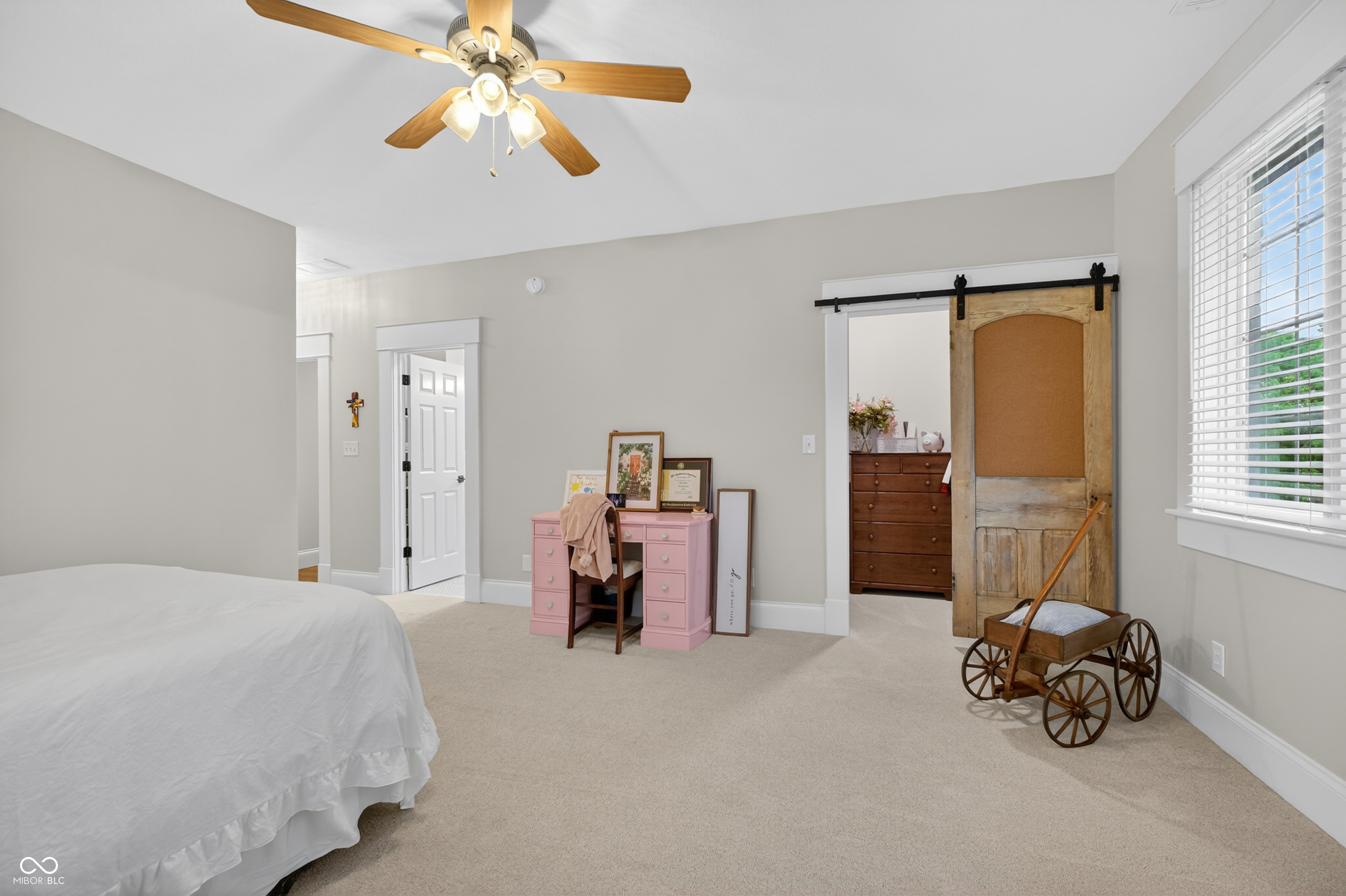 Bedroom with a pink desk, rustic sliding barn door, and wooden doll carriage.