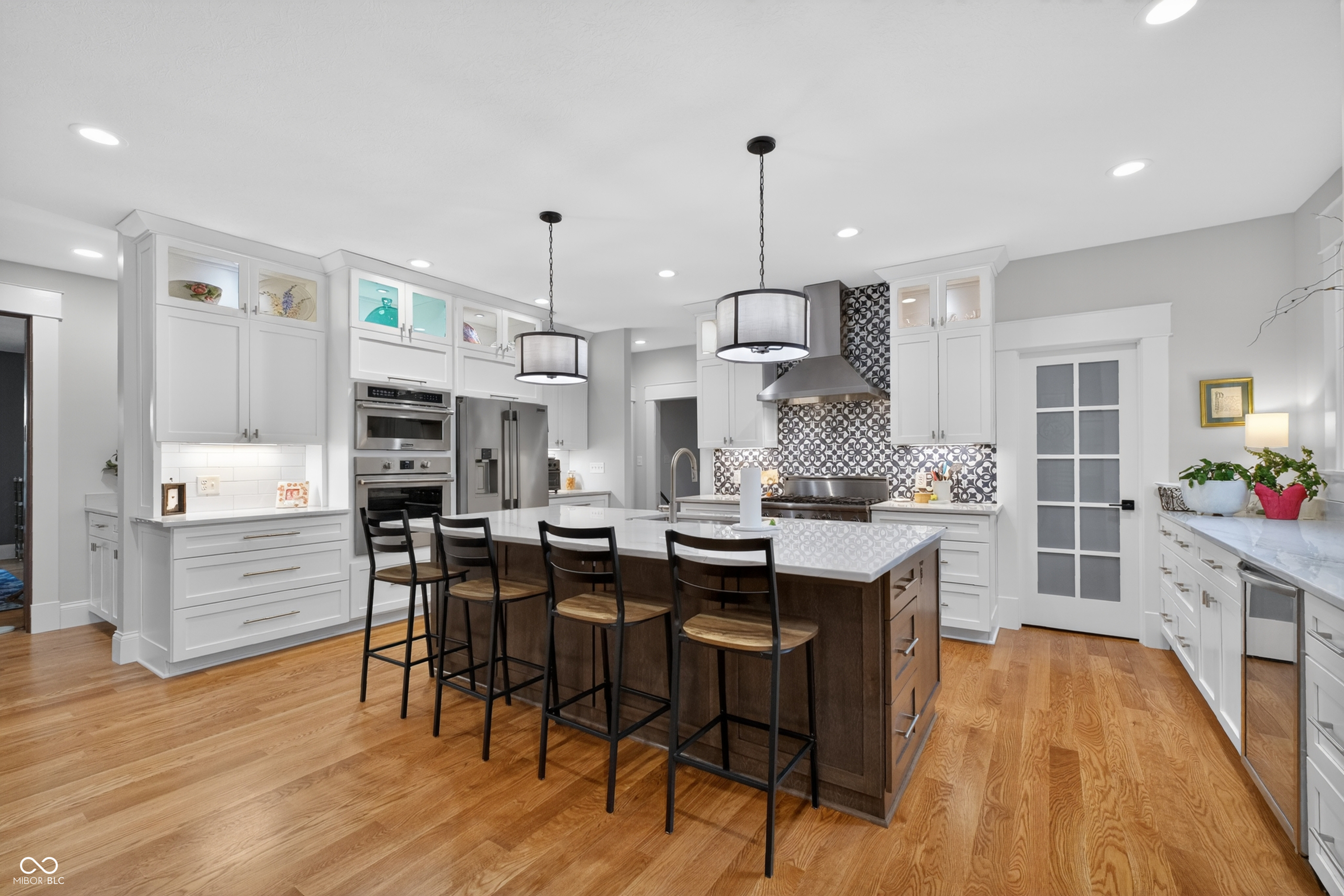 Bright kitchen with white cabinets, patterned tile backsplash, and a large island with bar stools.