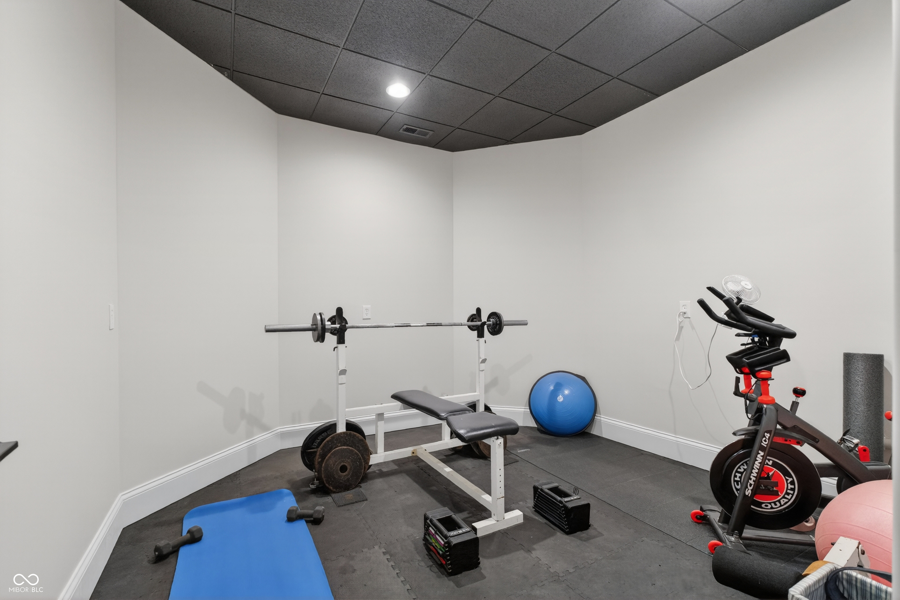 Home gym with a weight bench, barbell, stationary bike, and blue exercise mat.