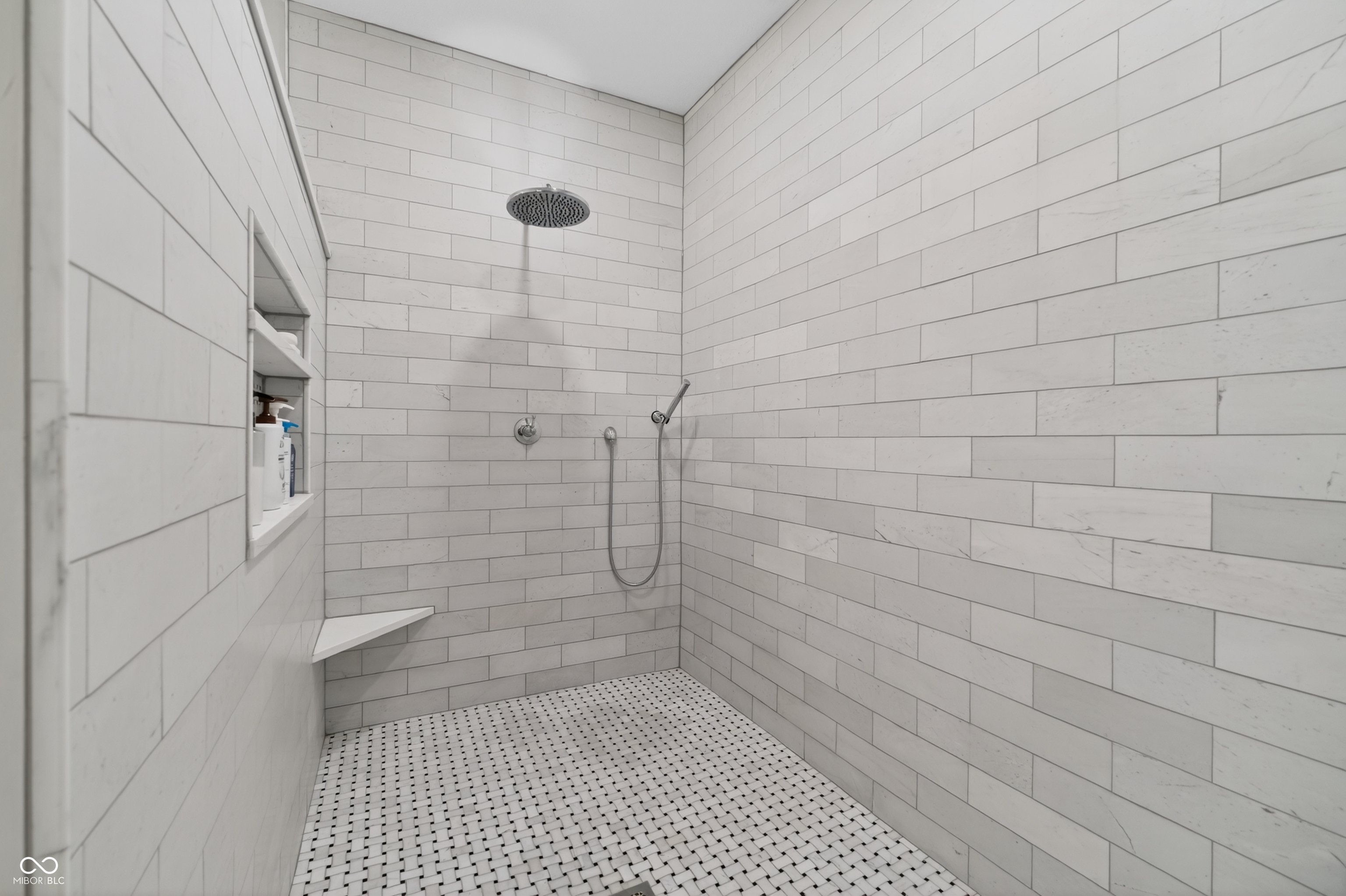 Walk-in shower with white tile, rain showerhead, handheld sprayer, built-in niche, and corner bench.