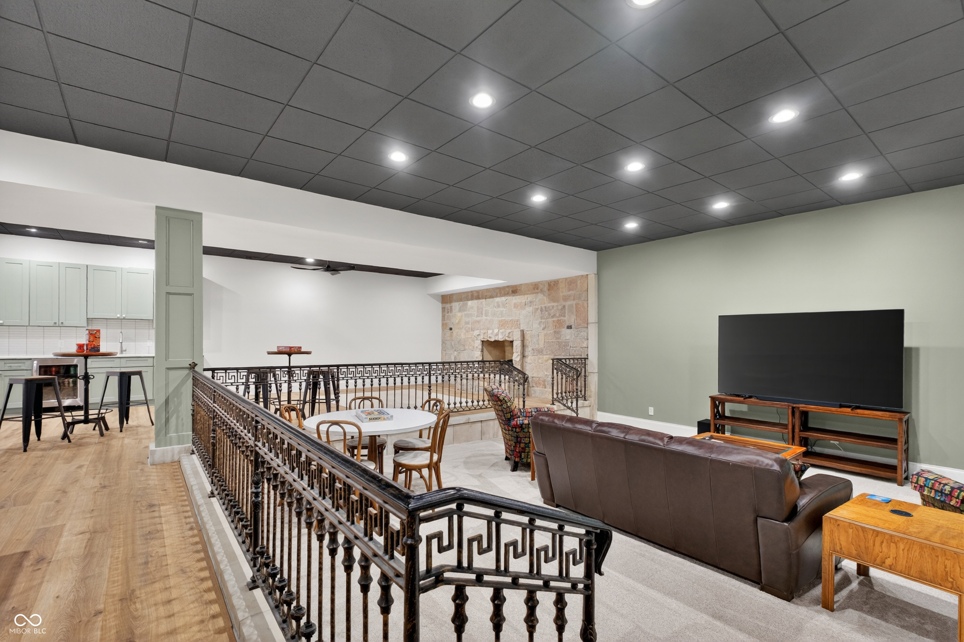 Furnished living area with a stone fireplace, leather sofa, television, and ornate metal railing.