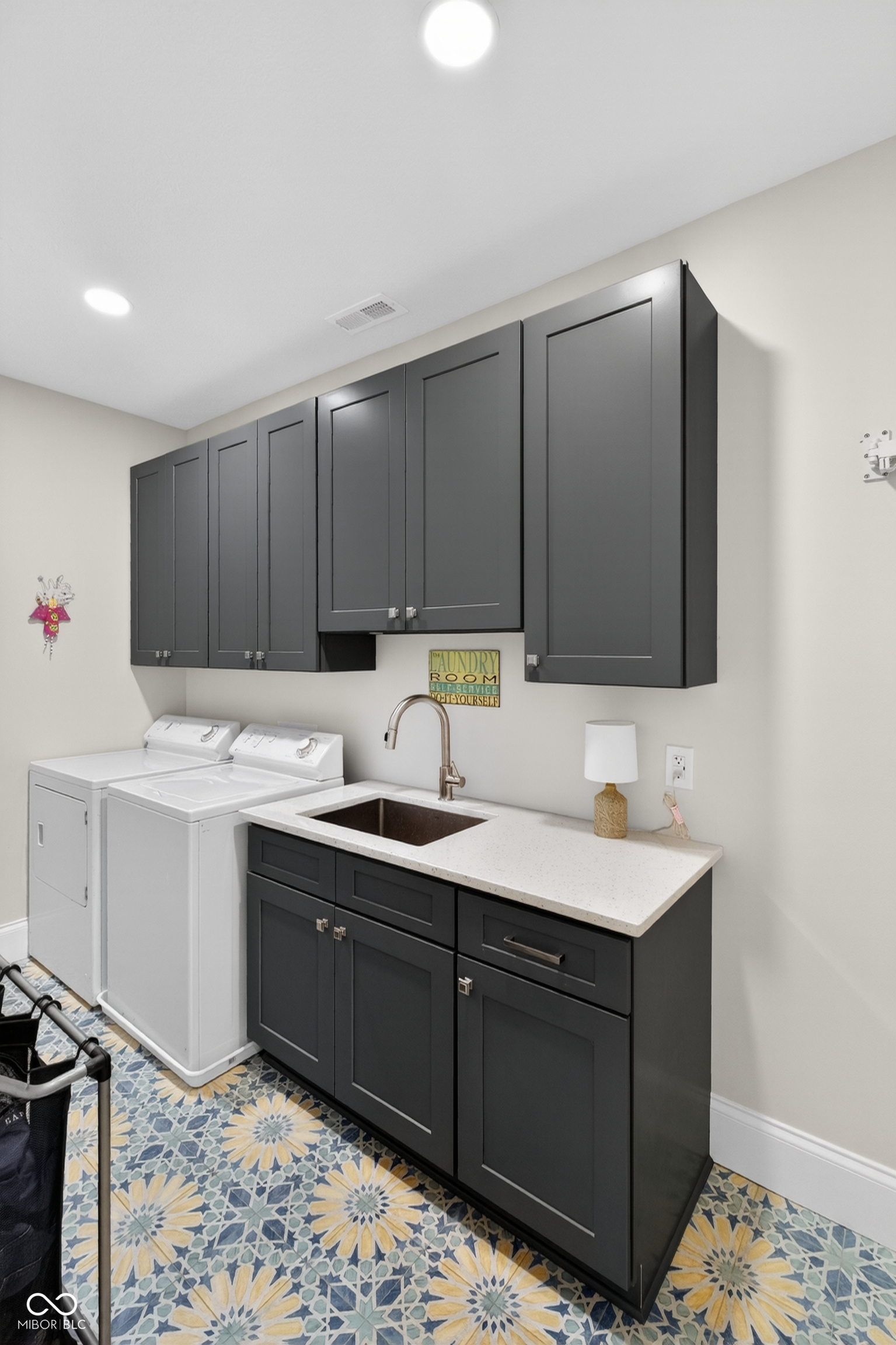 Laundry room with a washer and dryer, dark gray cabinets, utility sink, and patterned tile floor.