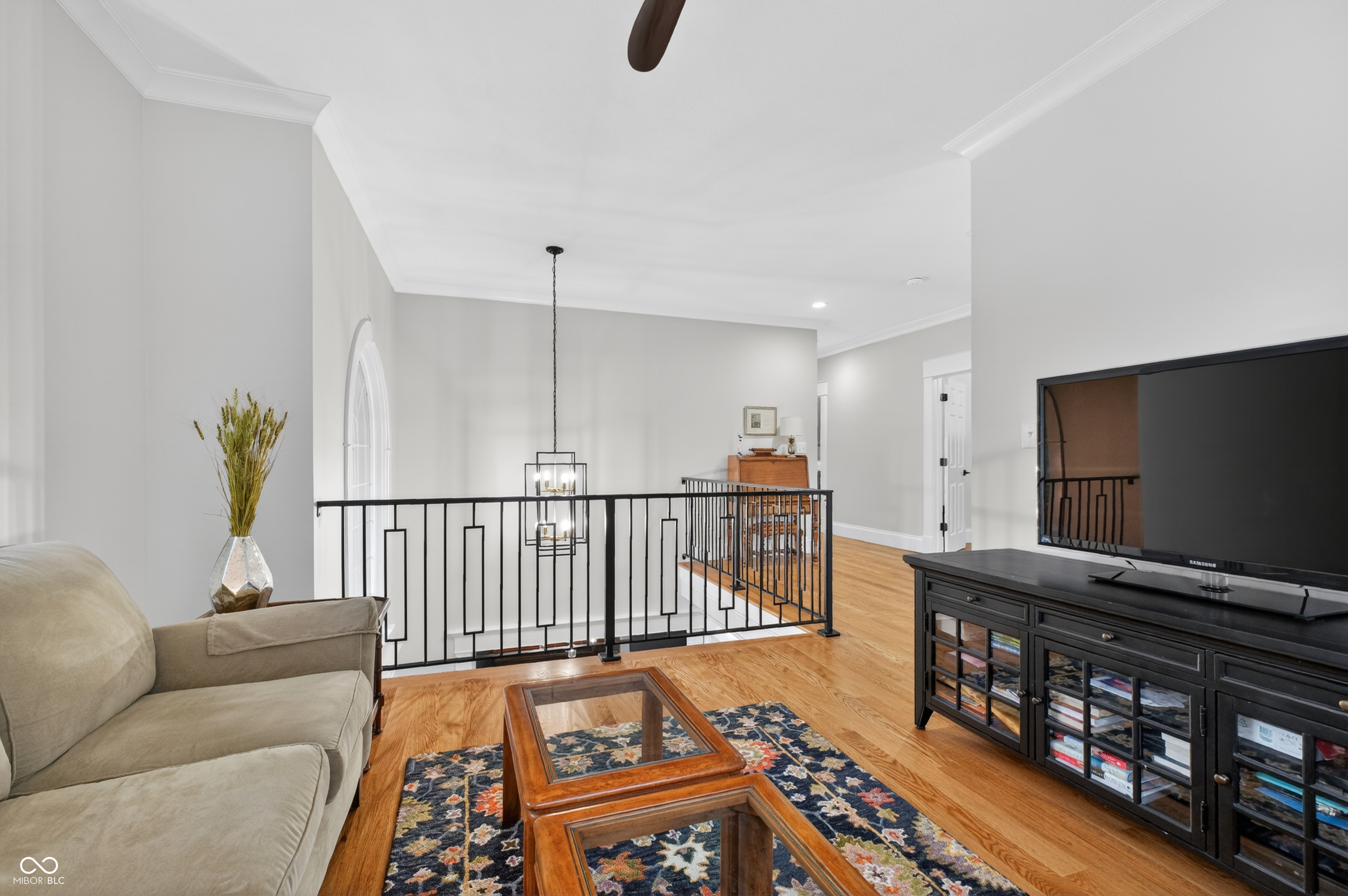 Upper-level living room with hardwood floors, a beige sofa, and a black railing around the open stairwell.