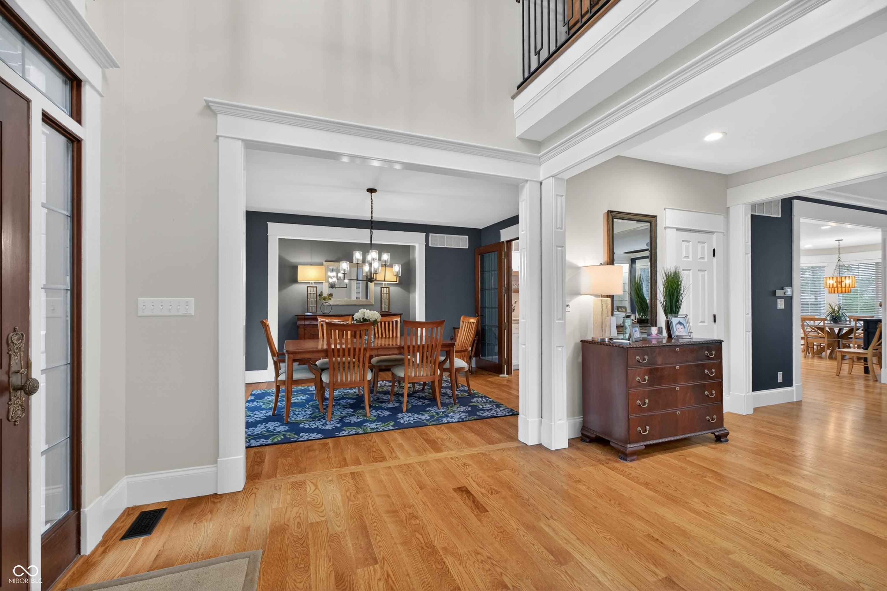 Formal dining room with a wooden table, blue patterned rug, chandelier, and hardwood floors.