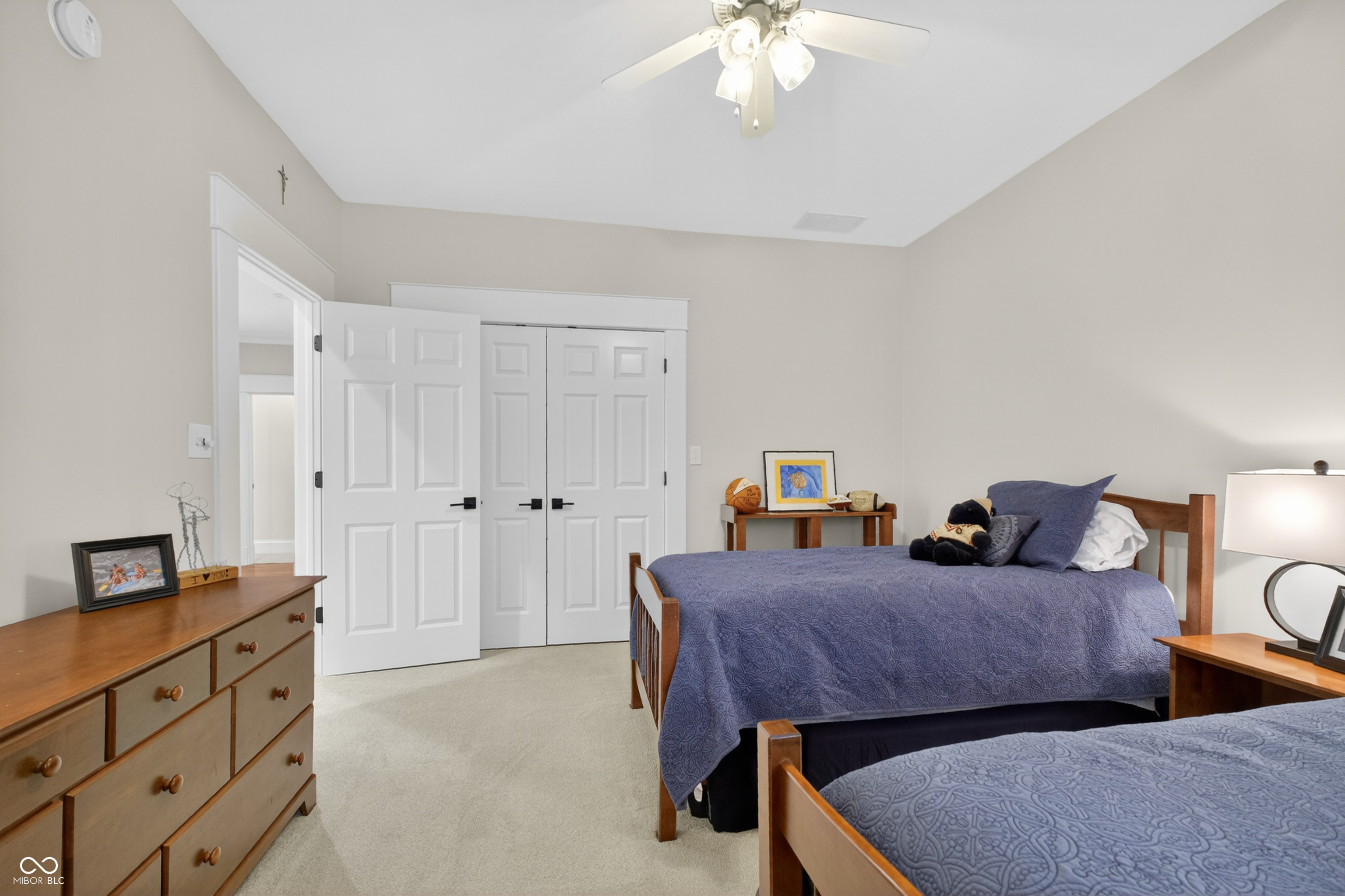 Bedroom with two wooden beds in blue patterned bedding and white double closet doors.