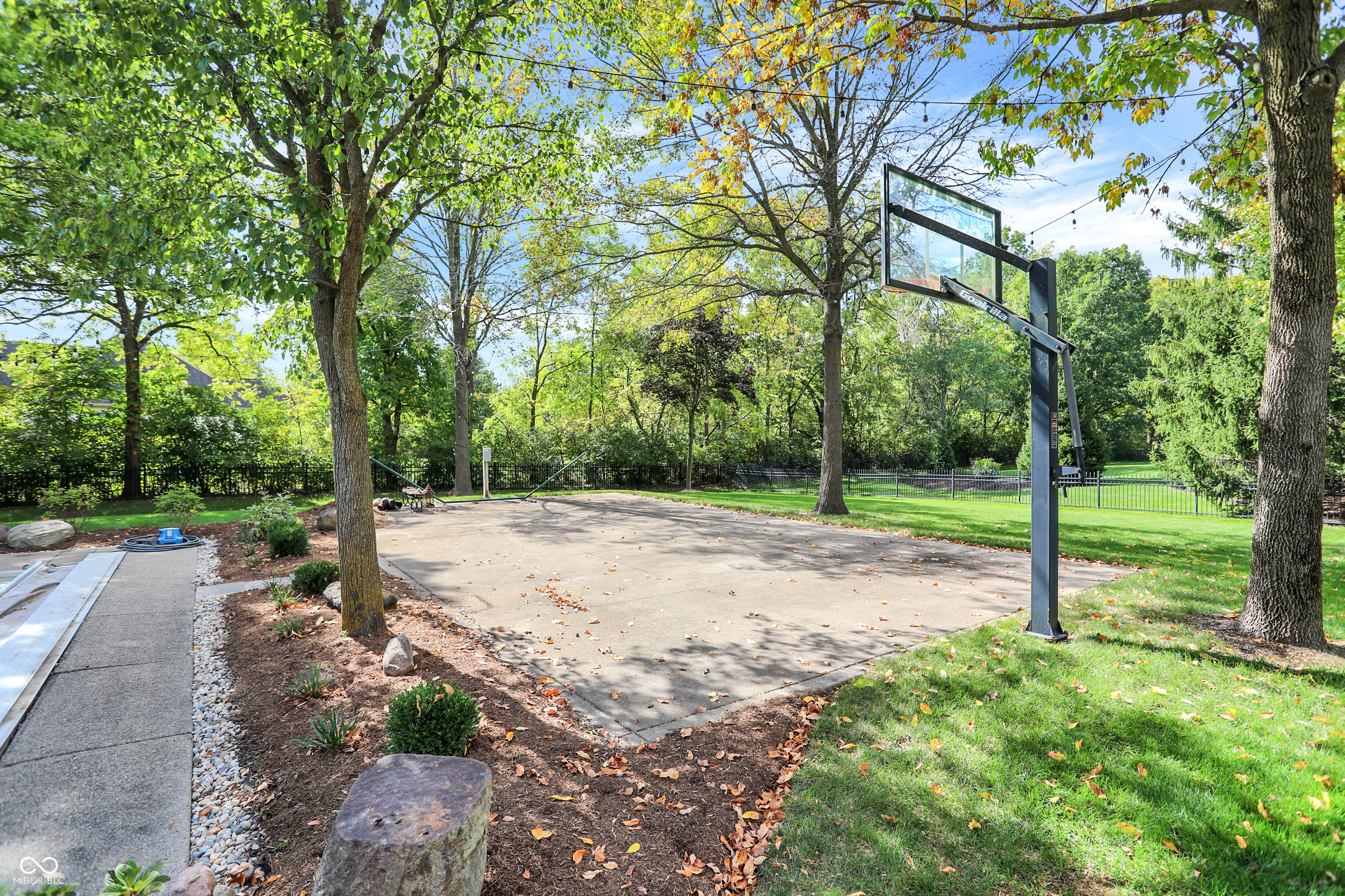 Backyard basketball court with a freestanding hoop, mature trees, and landscaped garden beds.