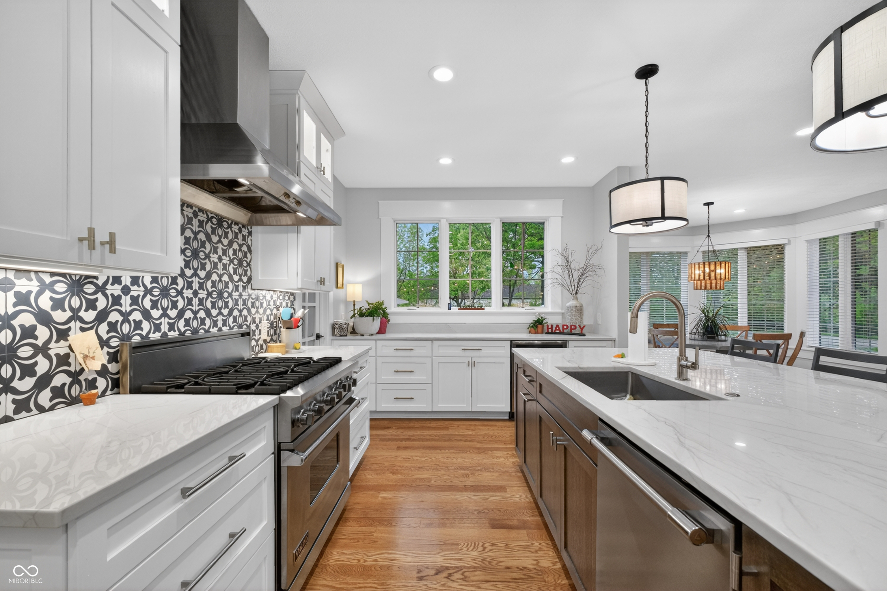 Kitchen with patterned backsplash, stainless steel range, and large island beneath pendant lights.