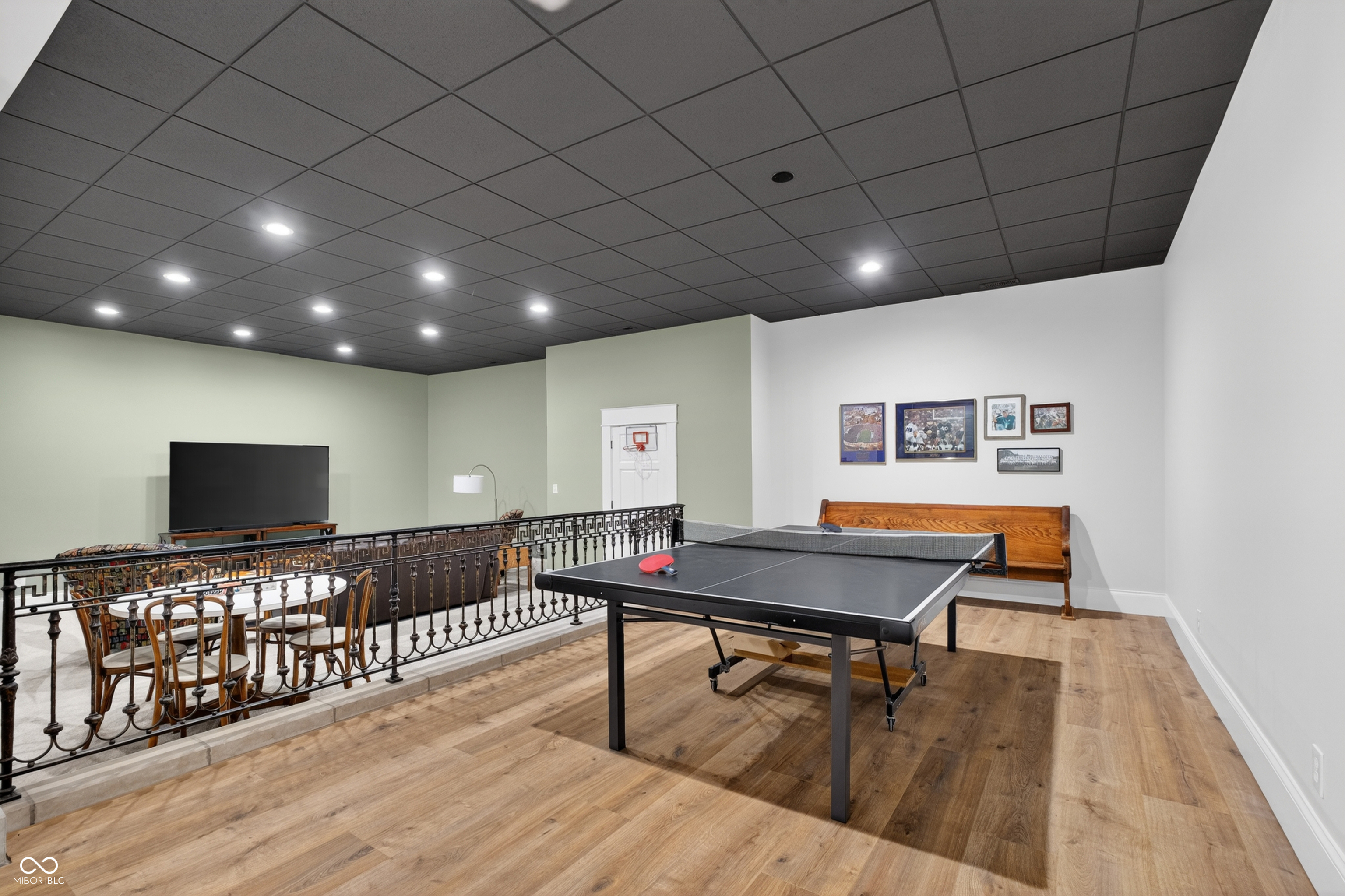 Recreation room with a ping-pong table, wooden bench, and railing overlooking a dining area.