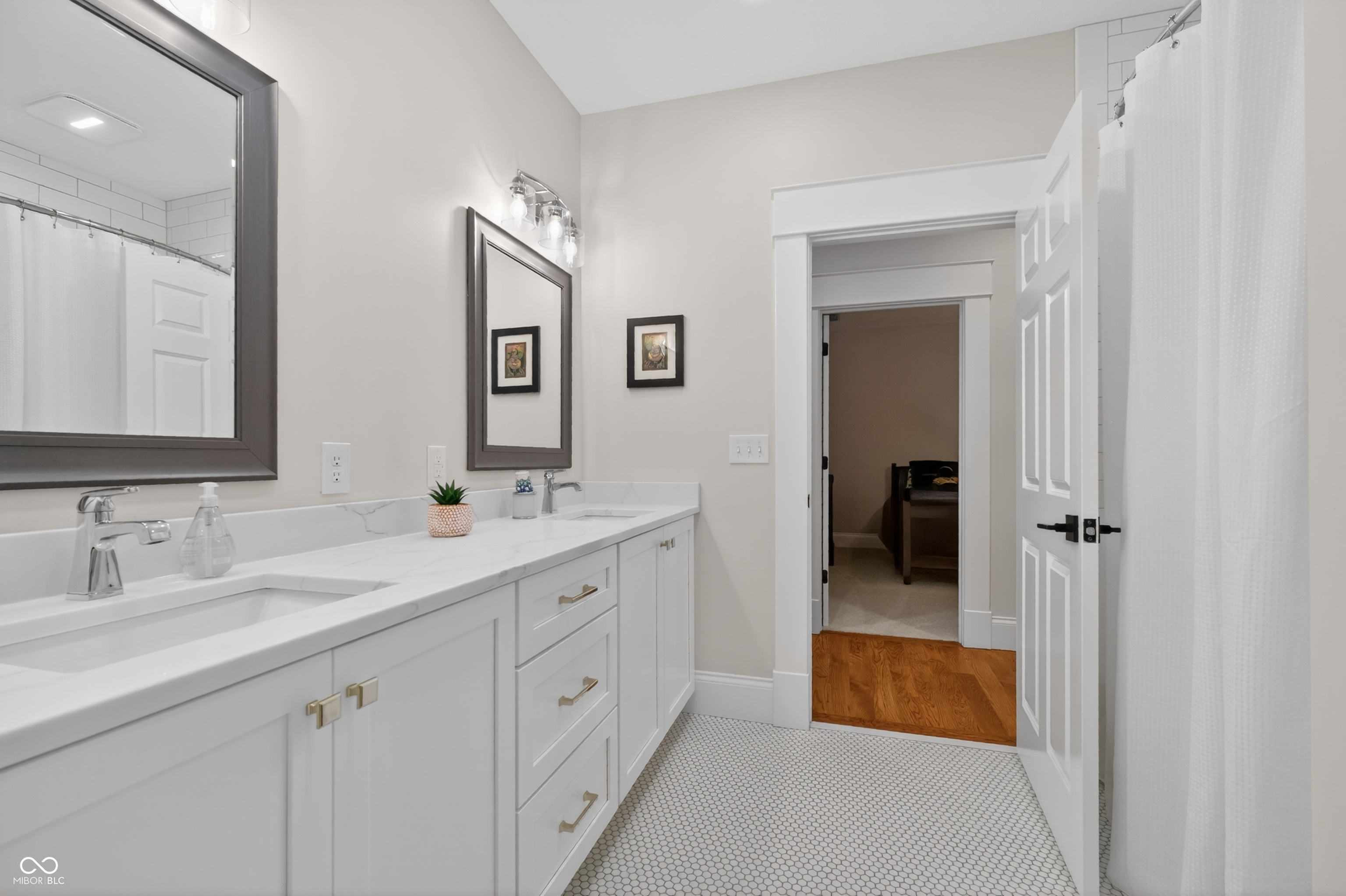 Bathroom with a long white vanity, patterned tile floor, and an open doorway to a bedroom.