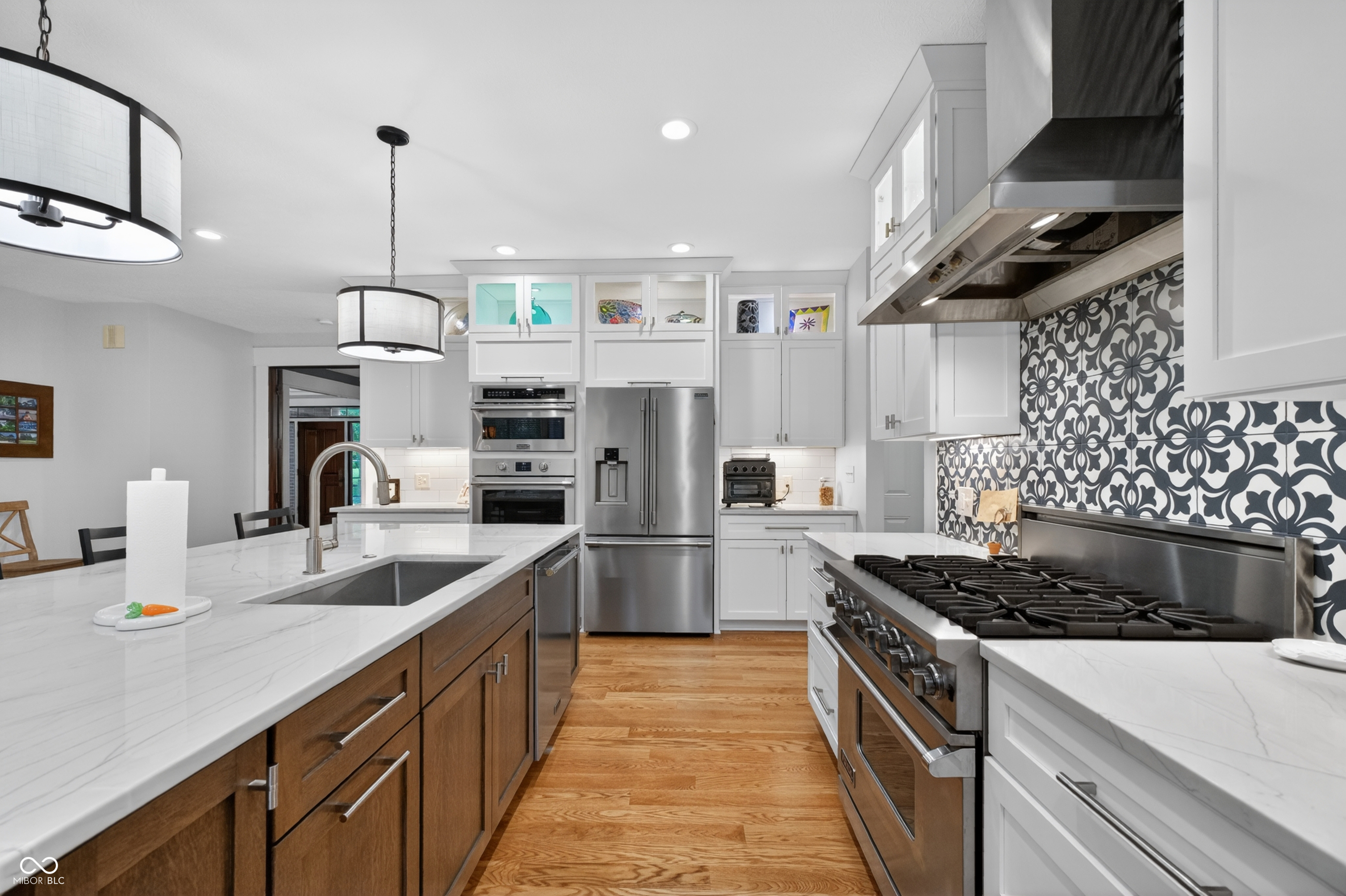 Kitchen with patterned tile backsplash, commercial-style range, marble-look counters, and wood-front island.