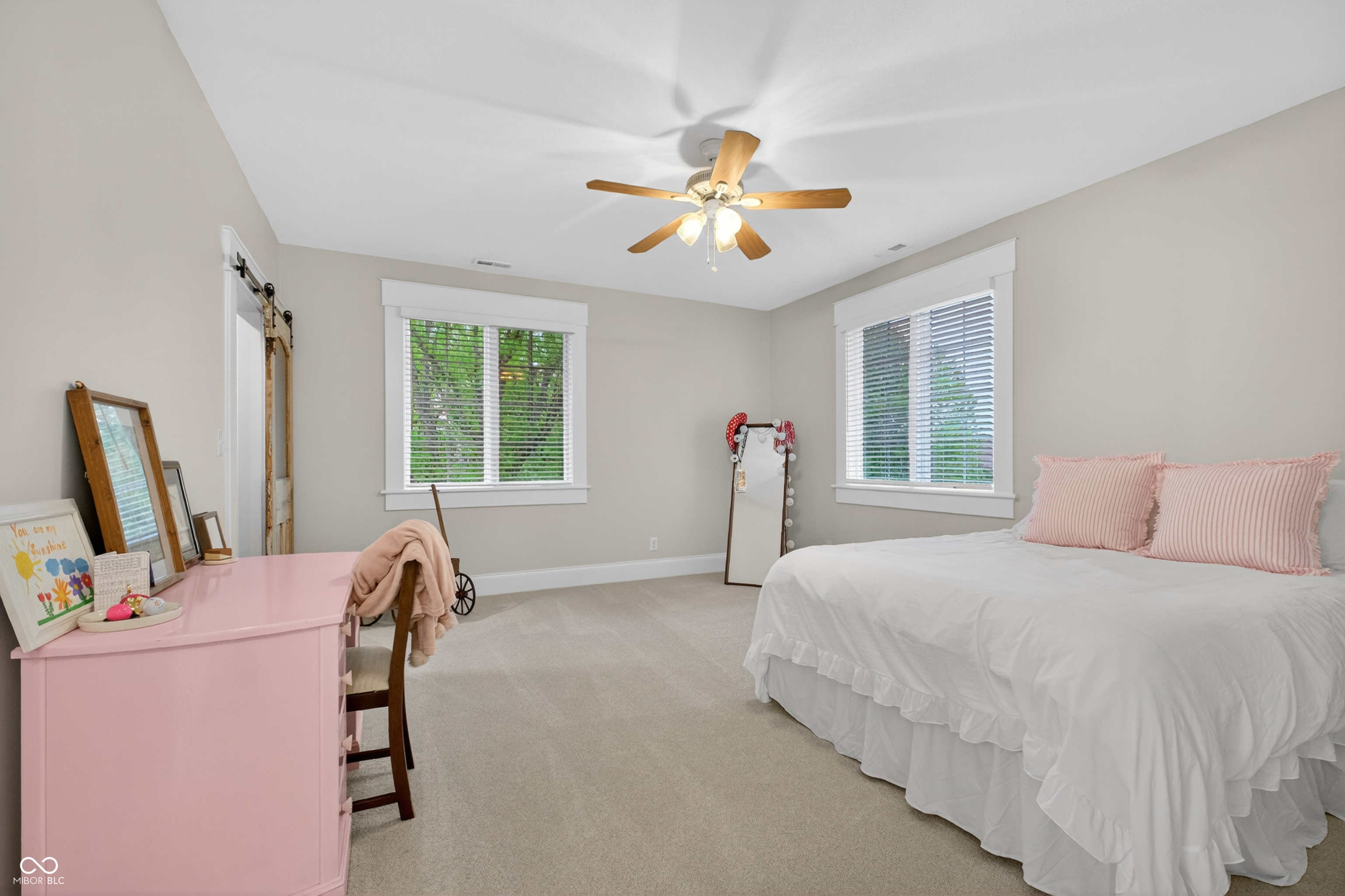 Bedroom with a white bed, pink striped pillows, and a pink dresser beneath two windows.
