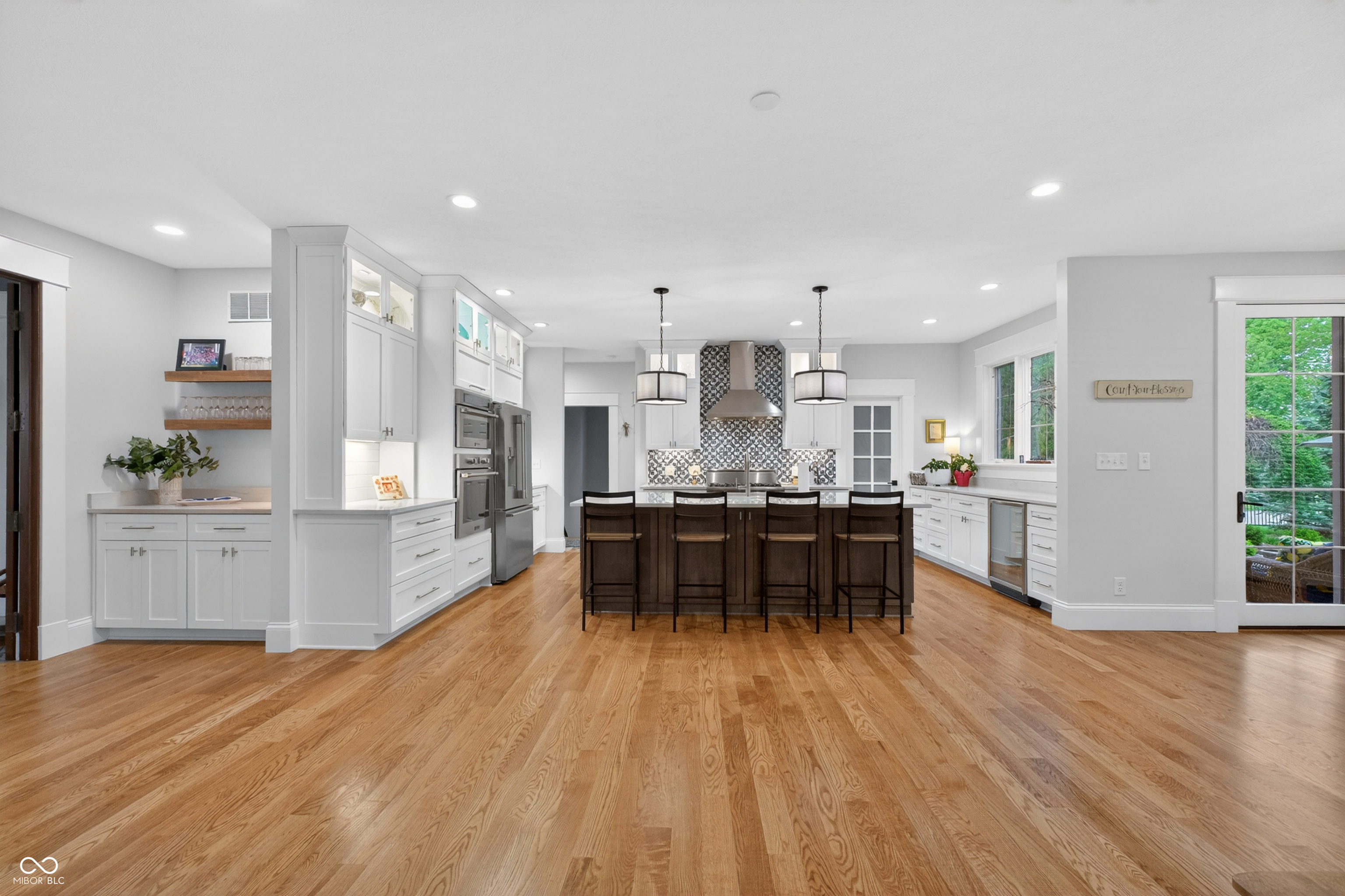 Bright kitchen with white cabinetry, patterned backsplash, dark island, and warm hardwood floors.