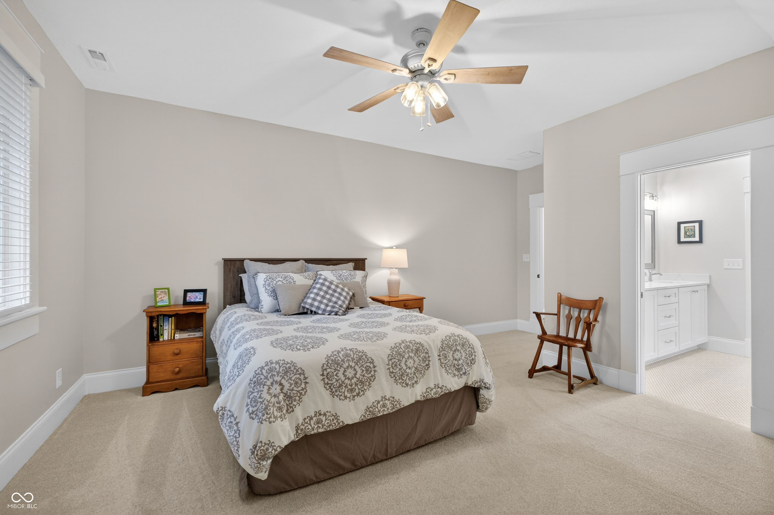 Furnished bedroom with a patterned bedspread, ceiling fan, and open doorway to the bathroom.