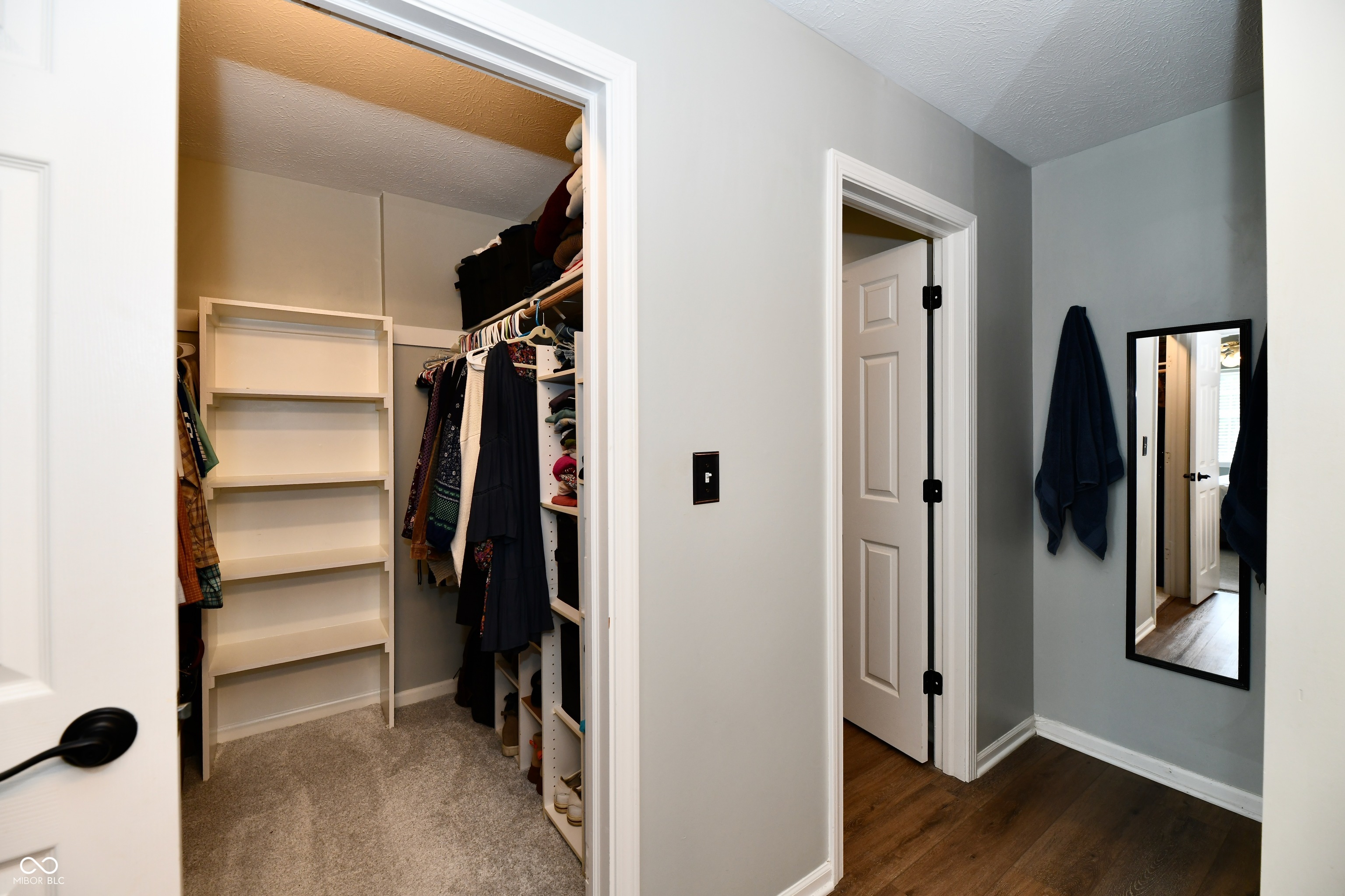 Walk-in closet with built-in shelving and hanging clothes beside a hallway mirror.