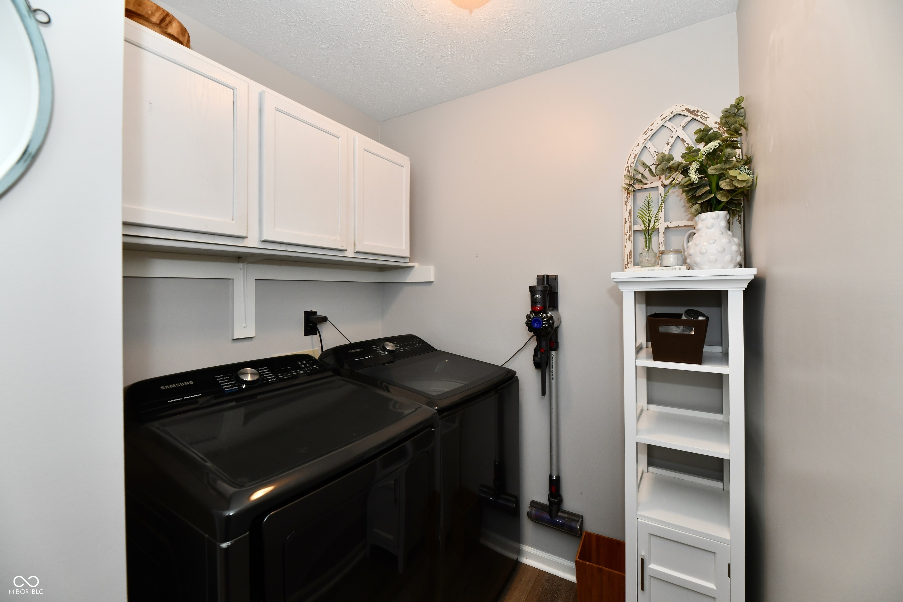 Laundry room with black washer and dryer, white cabinets, and a narrow decorated shelving unit.
