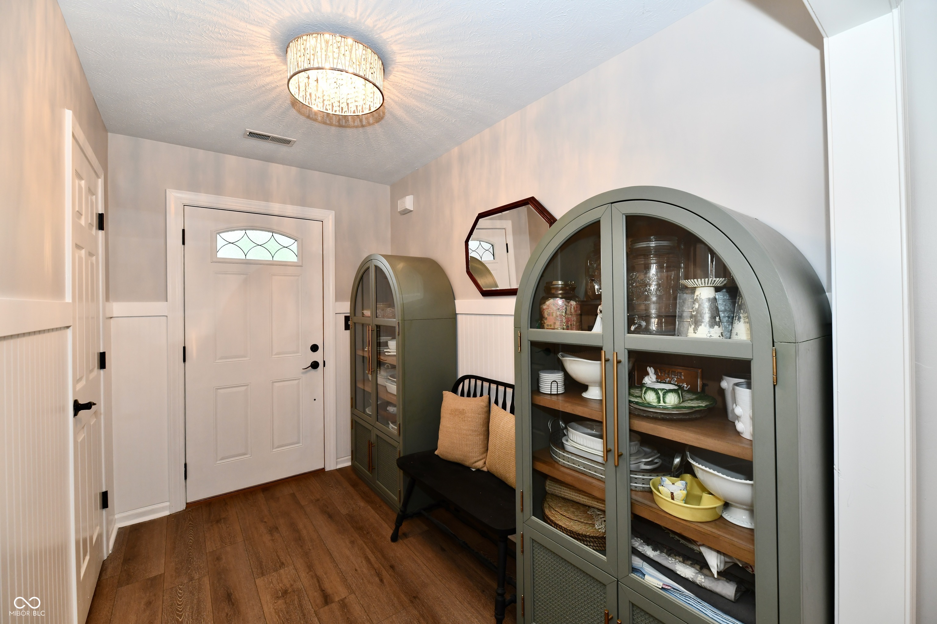Entryway with arched green display cabinets, a black bench, and a white front door.