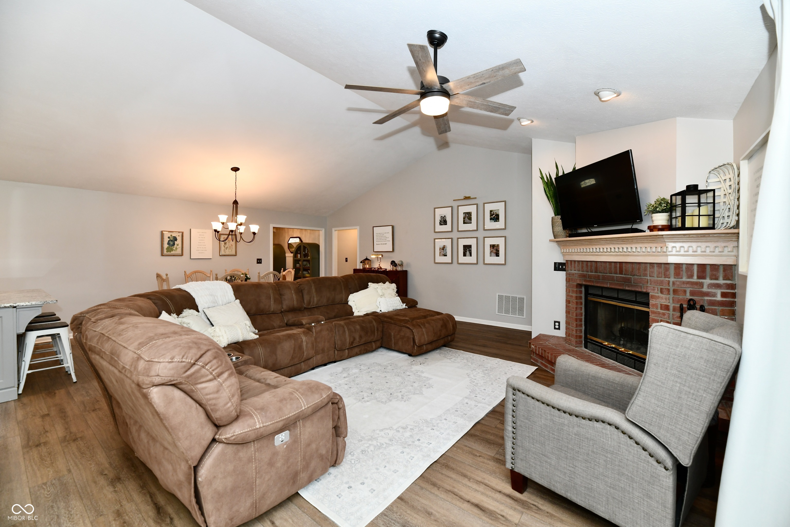 Living room with a large brown sectional, brick fireplace, and vaulted ceiling with a ceiling fan.