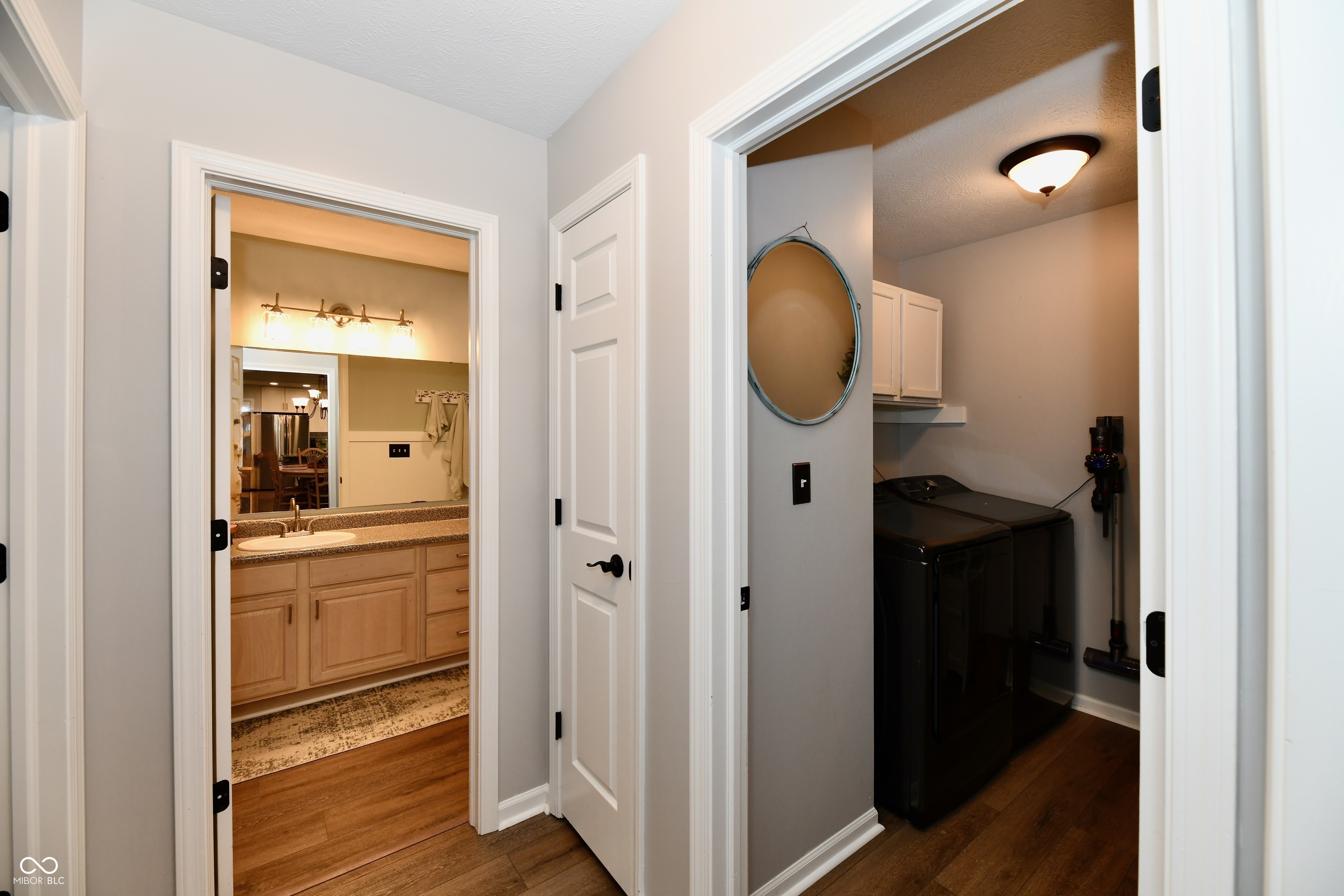 Hallway between a bathroom with a wood vanity and a laundry room with black appliances.