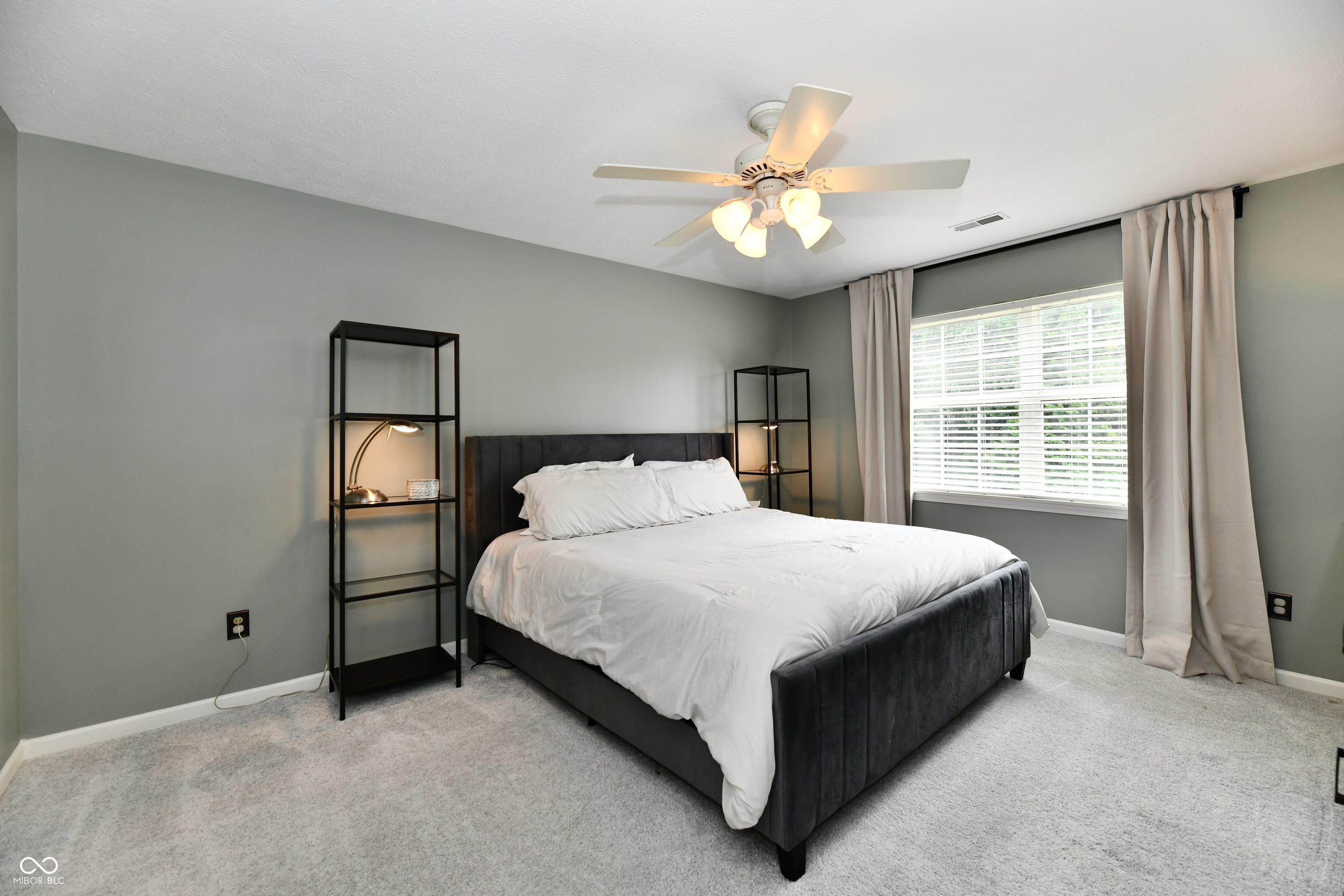 Bedroom with a dark upholstered bed, white bedding, gray walls, and a large curtained window.