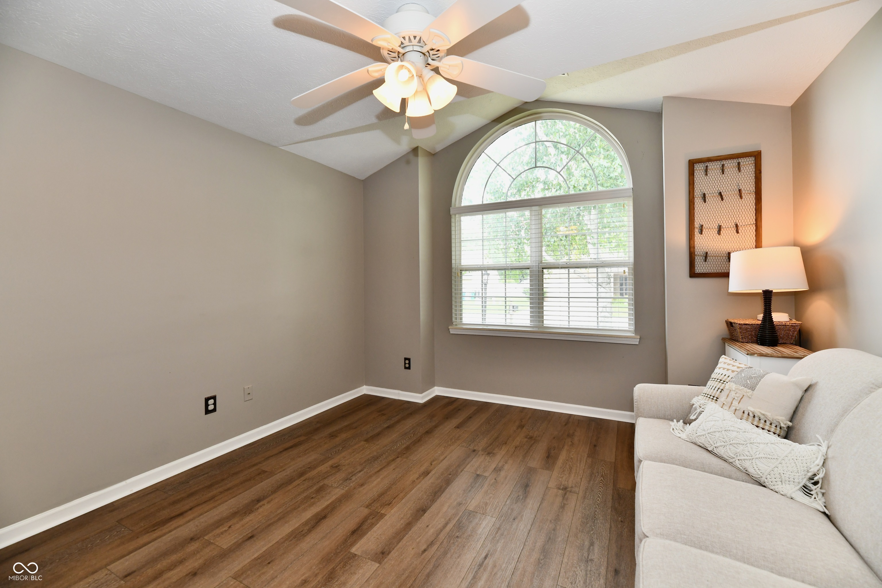 Sitting room with a white sofa, wood flooring, and a large arched window.