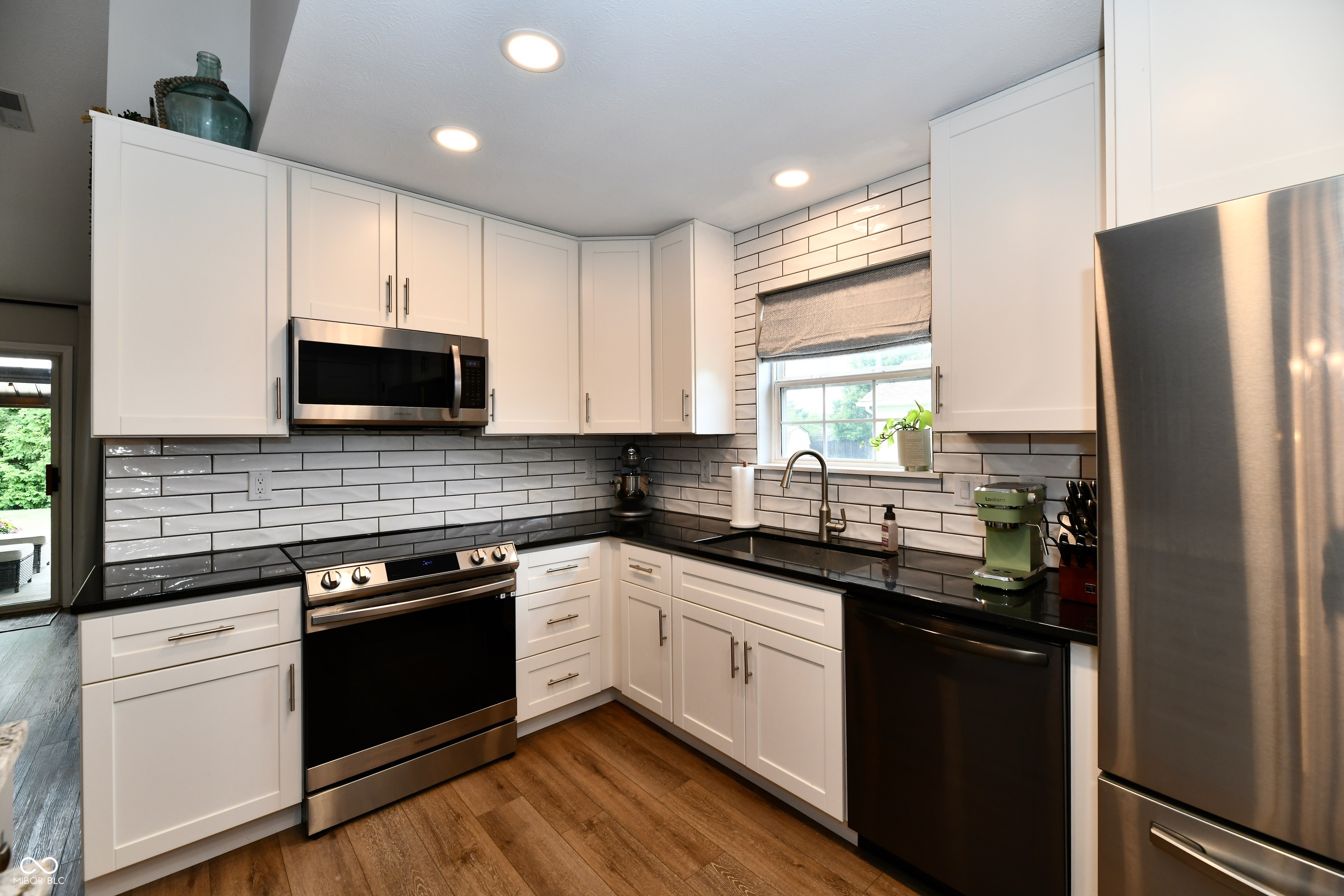Kitchen with white cabinets, black countertops, glossy subway-tile backsplash, and stainless steel appliances.