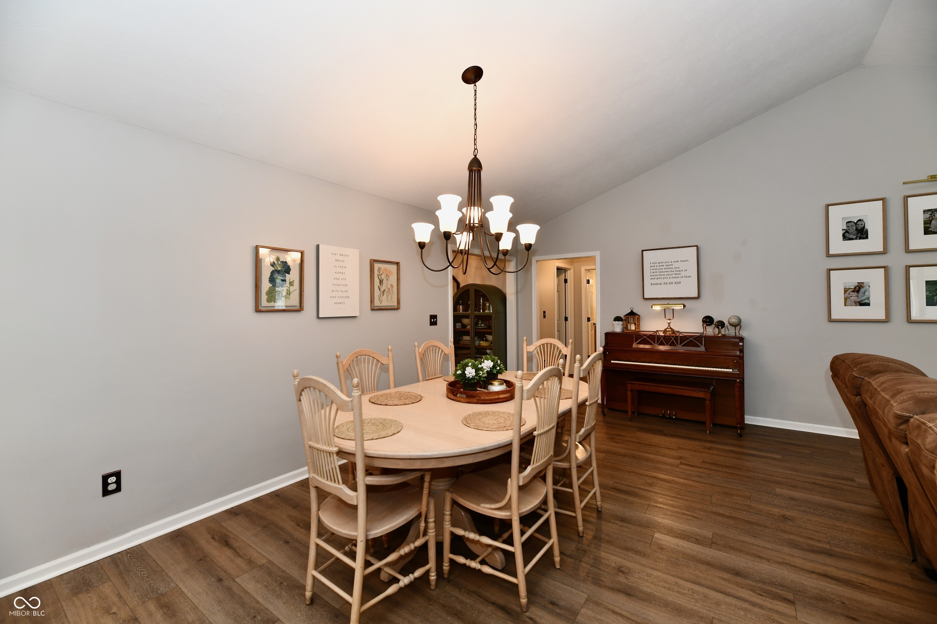 Dining room with a light wood table, chandelier, upright piano, and dark wood floors.