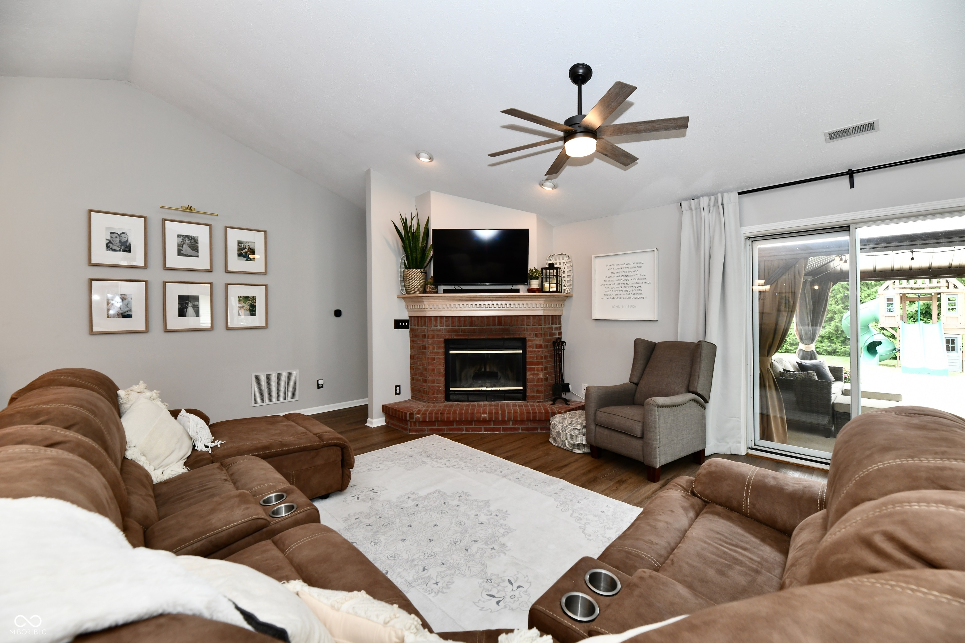 Living room with a brick fireplace, brown reclining sofas, and sliding doors to the backyard.