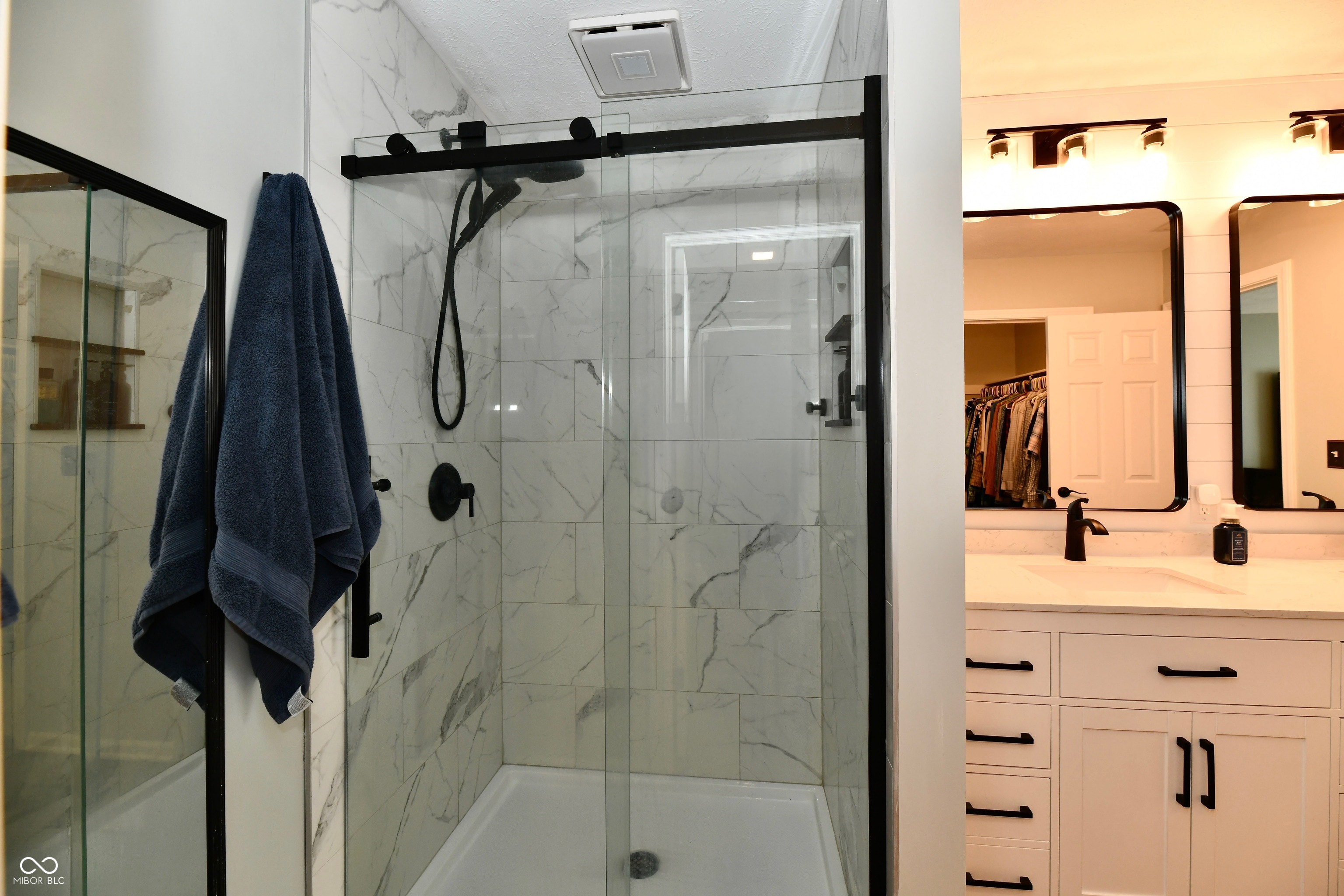 Bathroom with a marble-look walk-in shower, black fixtures, and a white vanity.