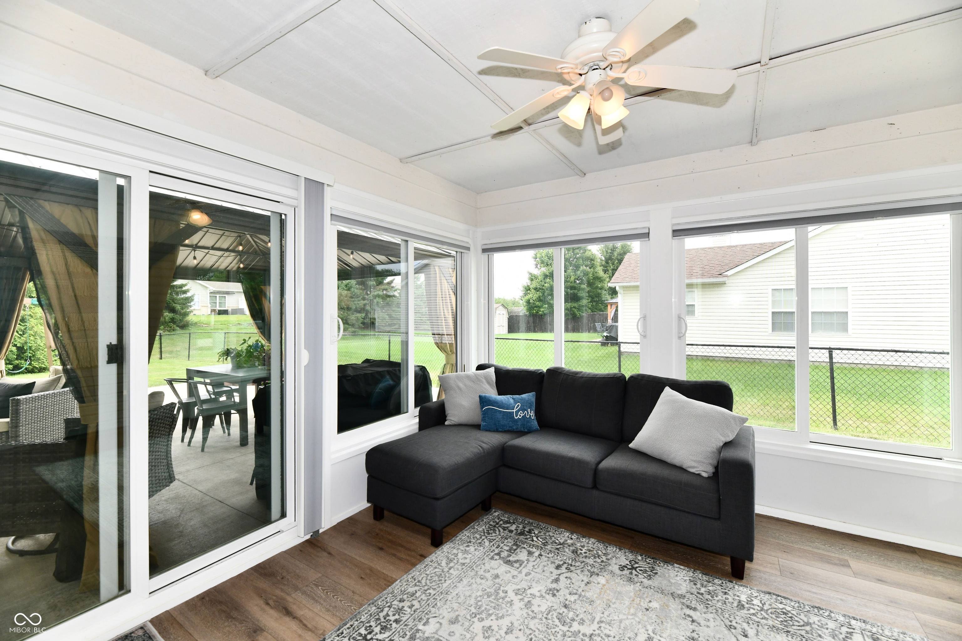 Sunroom with a dark gray sectional, large backyard-facing windows, and sliding doors to a covered patio.